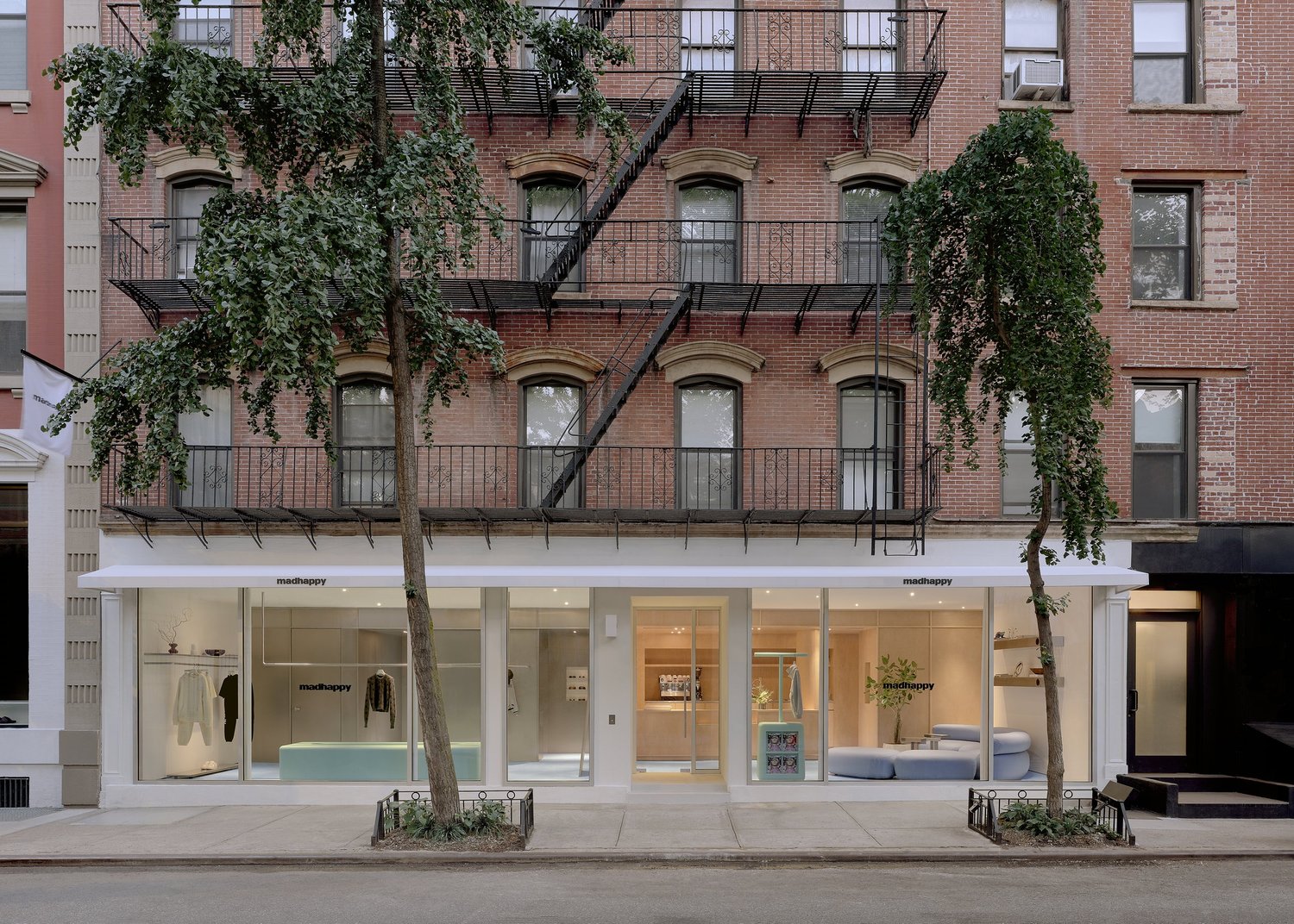 Street view of Madhappy New York Flagship store, with modern glass storefront set into a historic red brick building with fire escapes.