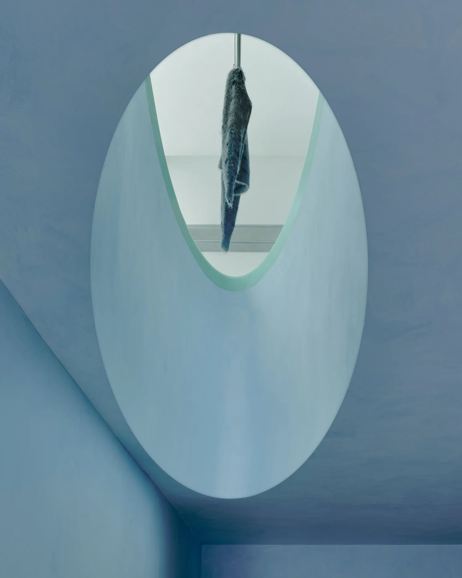 Interior detail at Madhappy New York Flagship showing a sculptural blue wall opening with a garment suspended from a ceiling-mounted rack.