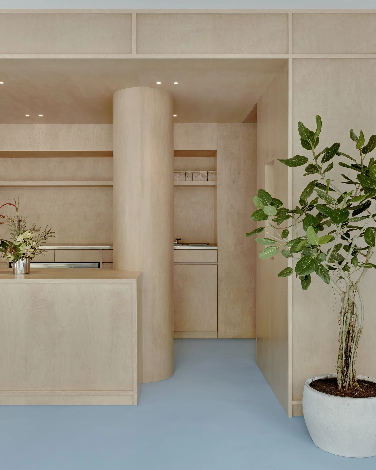 Interior of Madhappy New York Flagship store with light wood cash wrap counter, cylindrical column, and pale blue floor.