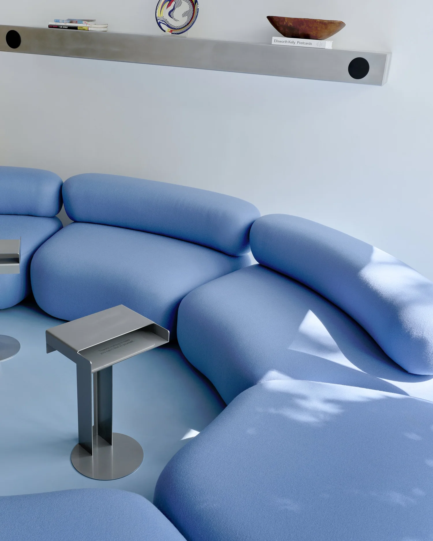 Detail of Madhappy New York Flagship lounge area with sculptural blue modular sofa, metal side tables, and floating wall shelf.