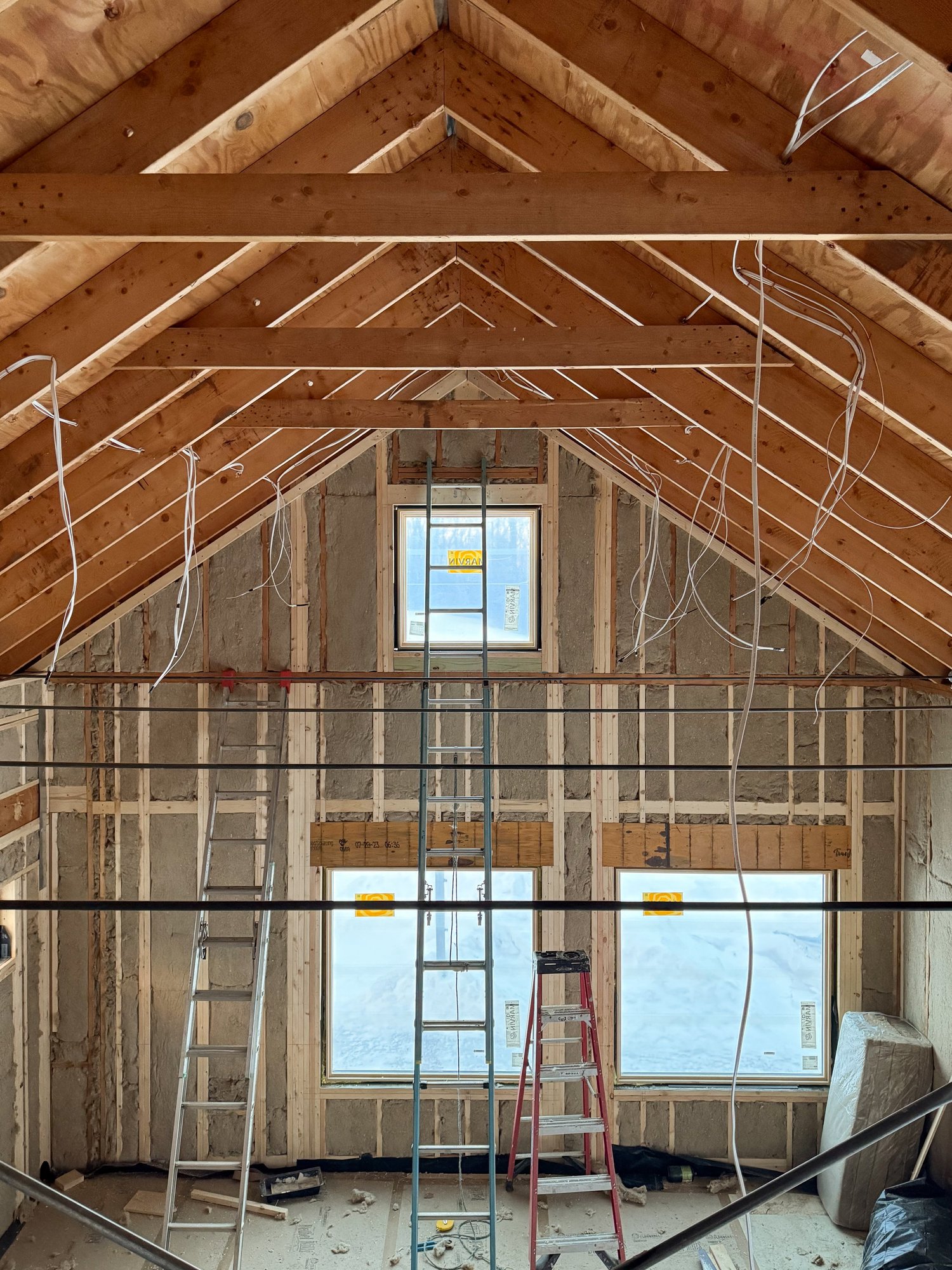 Interior under construction at Barnard Barn showing exposed roof framing, wiring, and insulation with a central ladder extending to a loft opening.