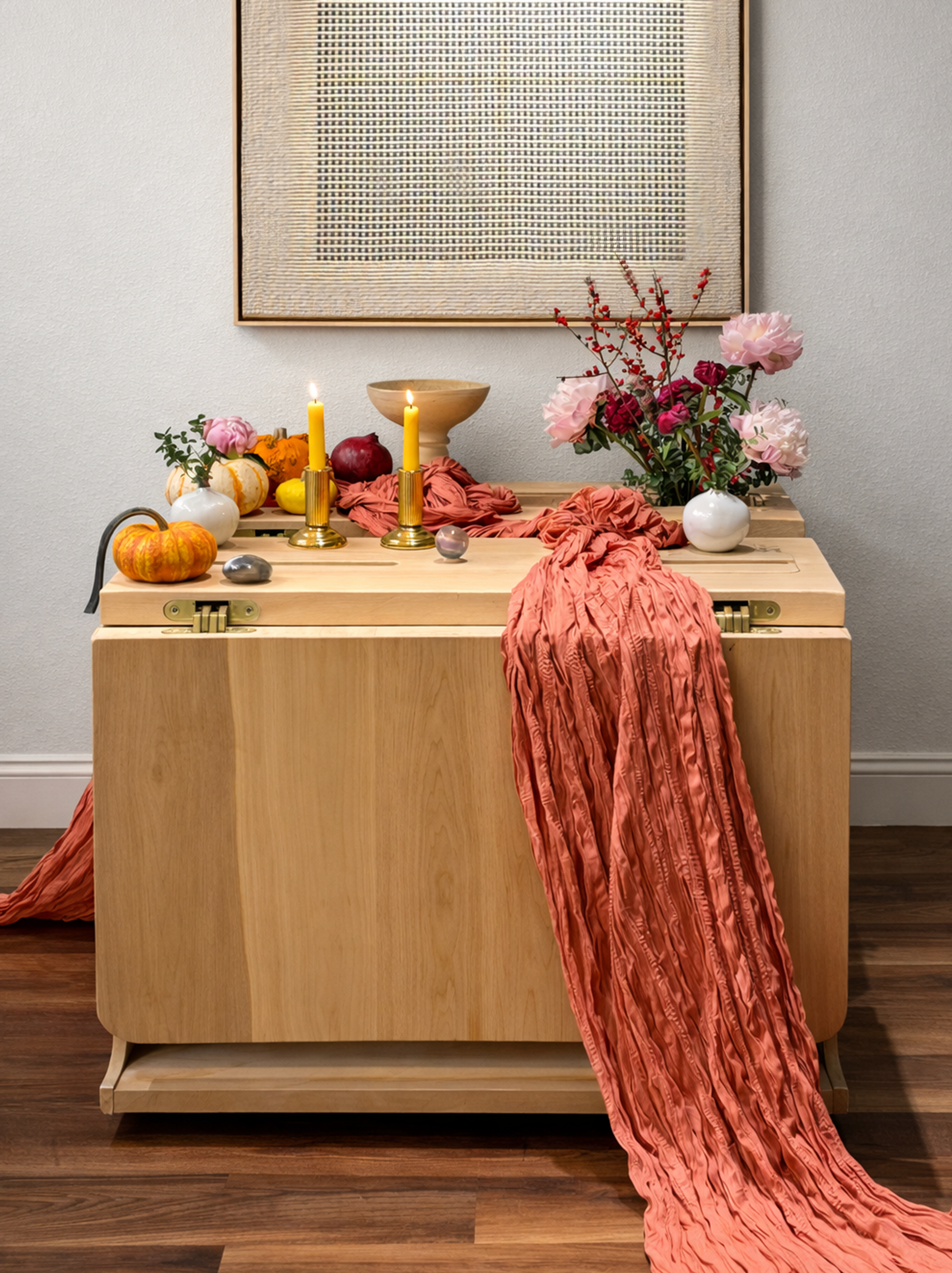 Folding Kenzan dining table in light maple wood, shown closed with integrated linear ikebana opening, styled with flowers, candles, fruit, and a draped textile