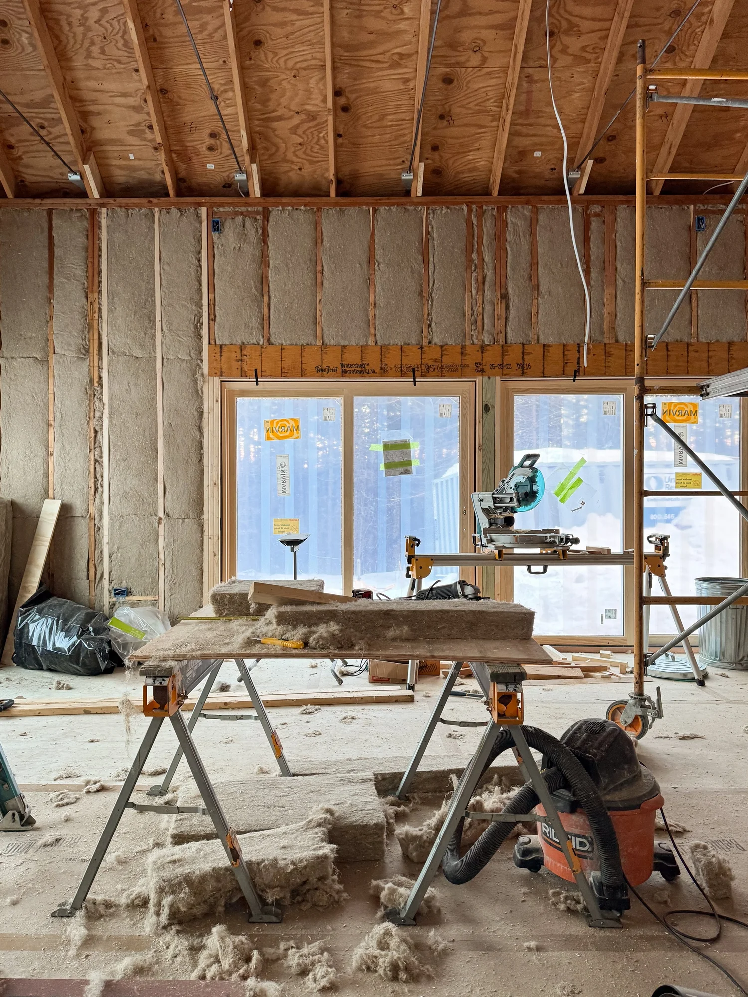 Construction site view of Barnard Barn interior with exposed stud walls, hemp insulation partially installed, and tools on sawhorses in the foreground.