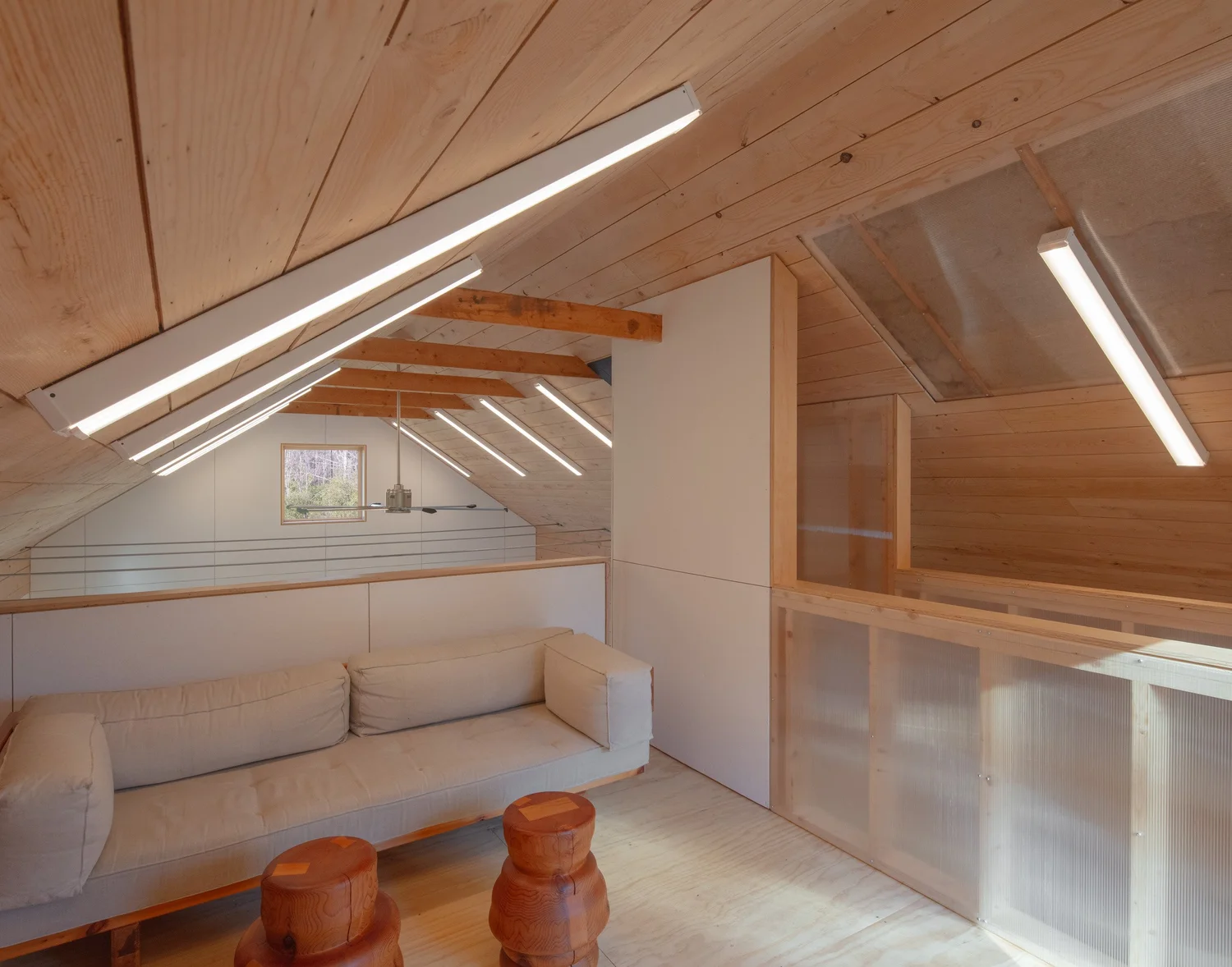 Interior view of Barnard Barn’s loft, with sloped wood ceilings, exposed rafters, linear strip lighting, and a white sofa against the railing. The loft overlooks the double-height barn space below.
