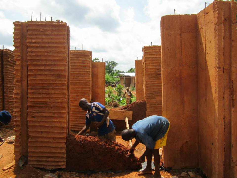 Workers building the Mudhouse with completed cast-earth pillars during construction.