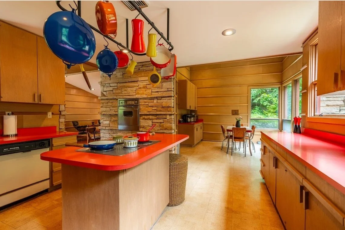 Kitchen interior of the Duncan House designed by Frank Lloyd Wright, featuring warm wood cabinetry, red countertops, integrated storage, and a central workspace within an open Usonian plan.