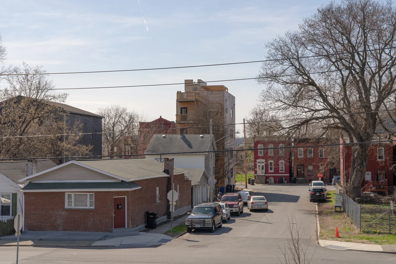 Neighborhood view looking toward Swift Street Residences in Troy, New York, with the four-story wood-clad building visible beyond brick rowhouses and parked cars.