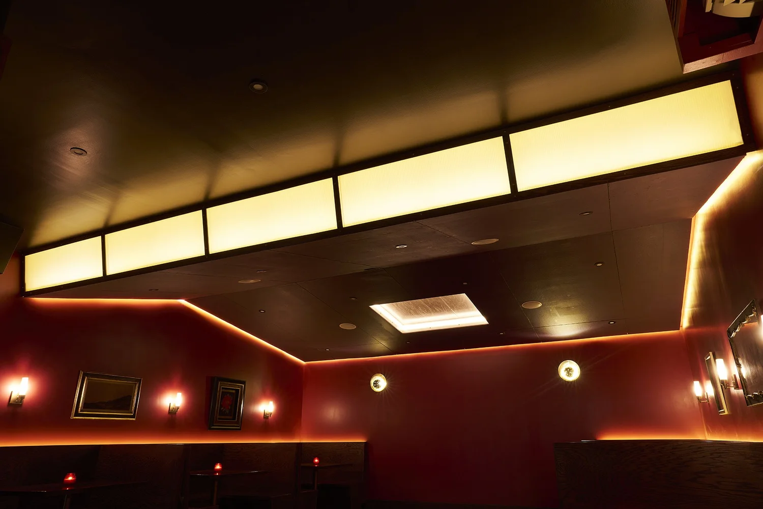 Lounge interior at Mr. Nancy’s with deep red walls, dim lighting, framed artwork, and glowing perimeter light detail.
