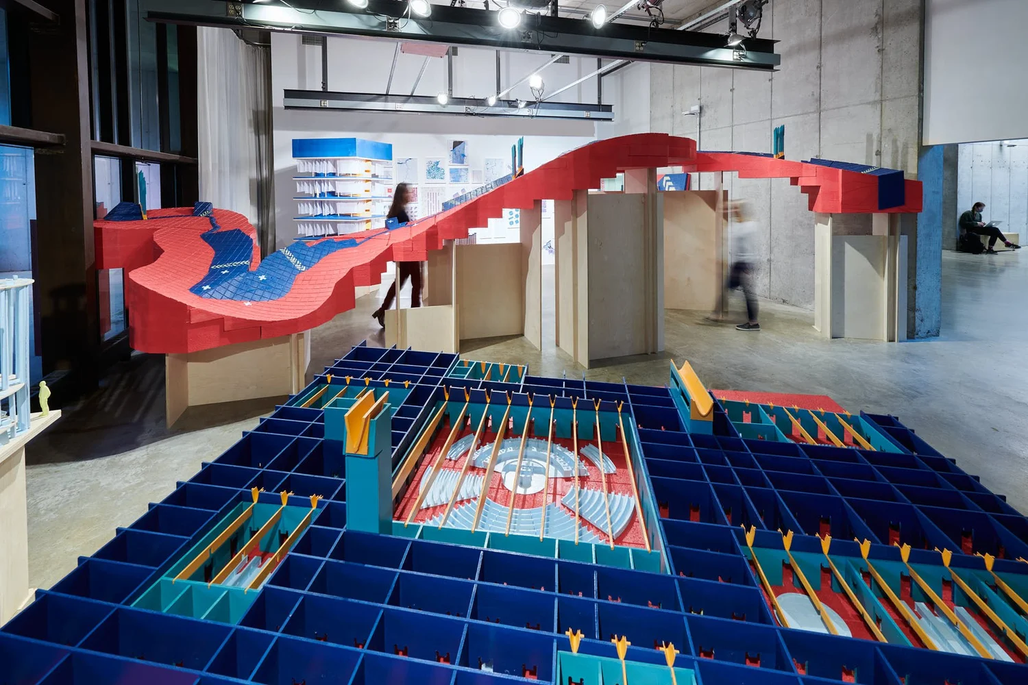 Exhibition view of the Great Lakes Expedition, featuring colorful architectural models with red, blue, and yellow modular components arranged across a gallery space.