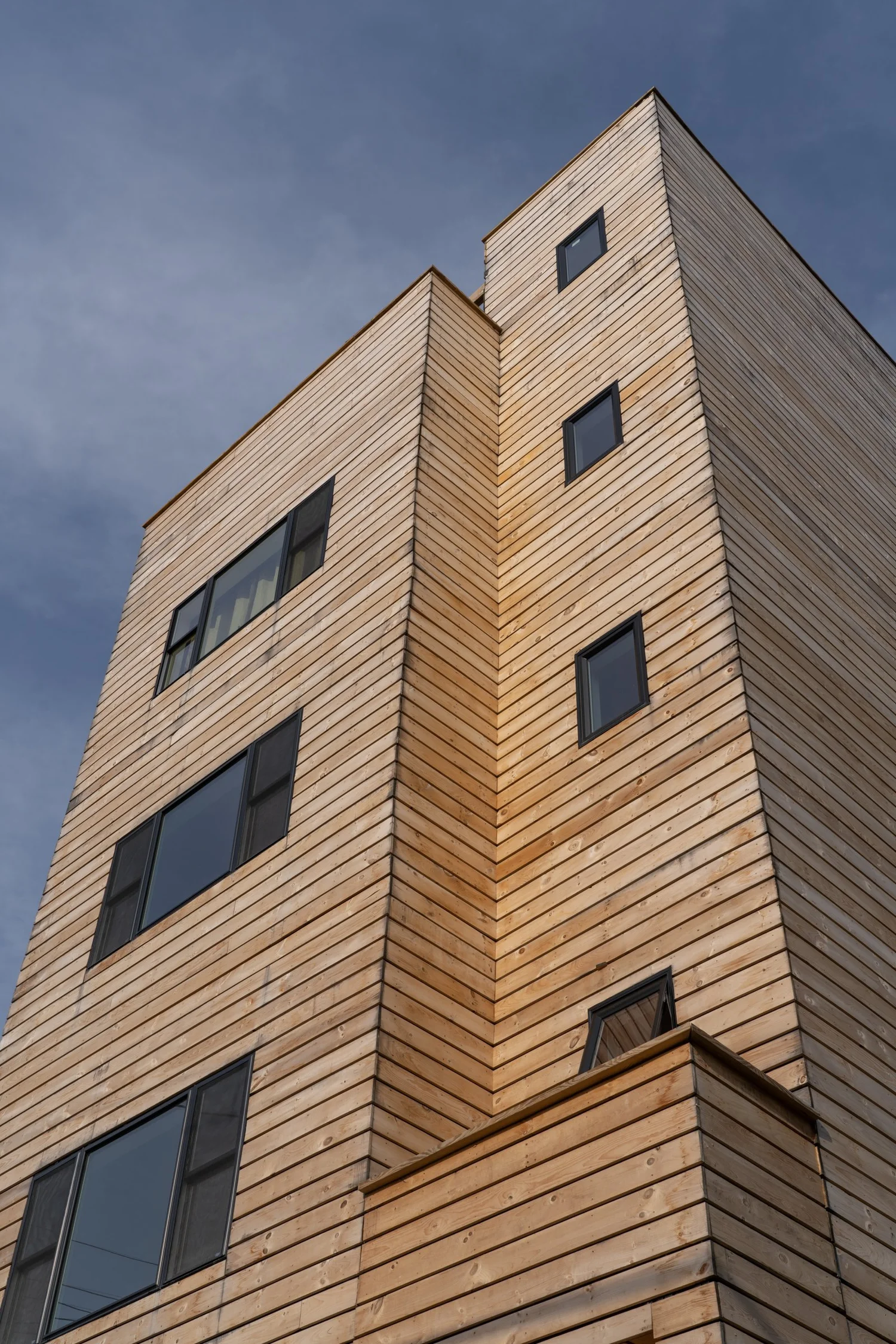Angled close-up view of Swift Street Residences, highlighting the wood cladding and modern window arrangement against a blue sky.