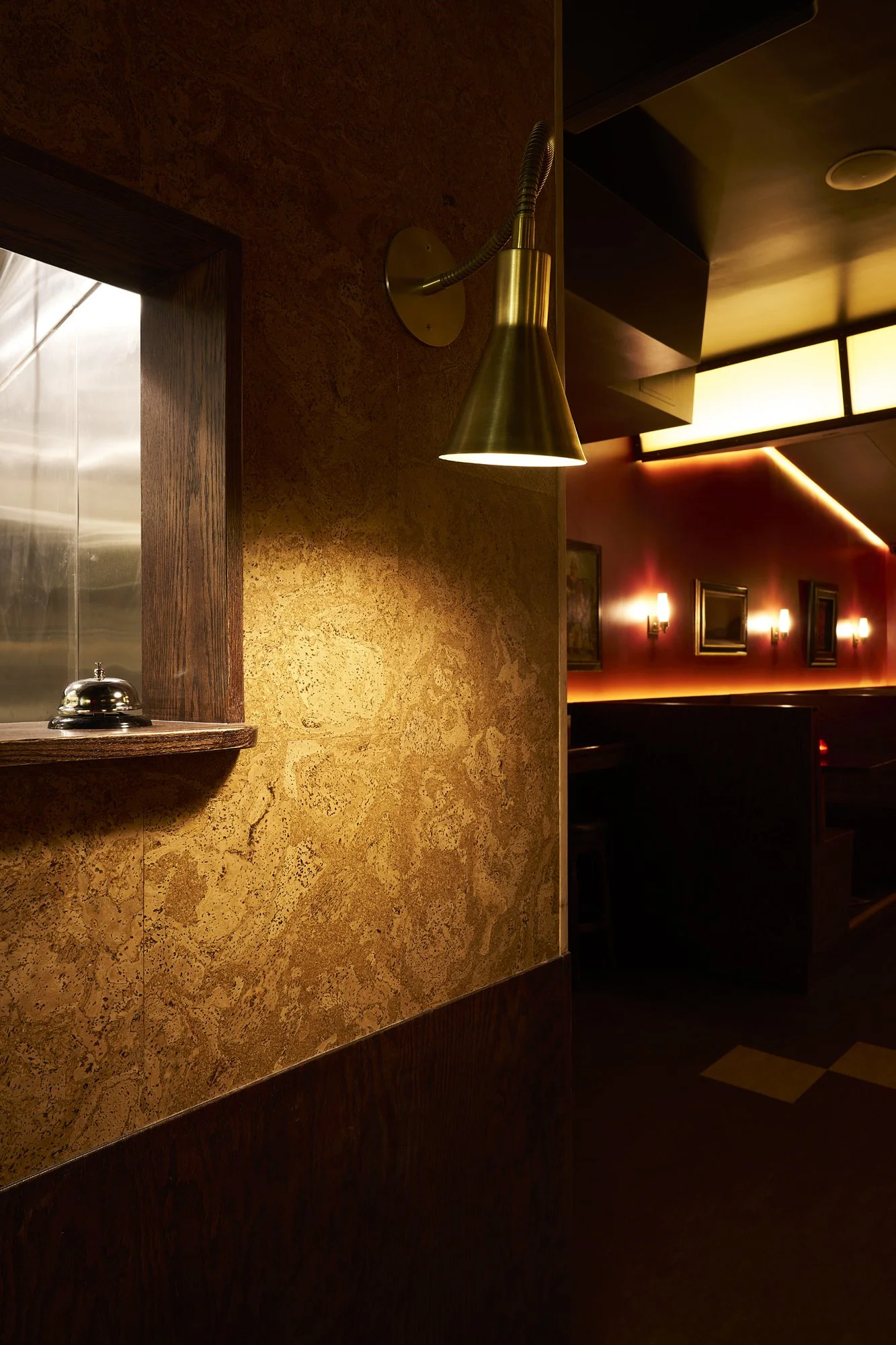Host station at Mr. Nancy’s with a brass wall sconce, cork-textured wall, and service bell niche overlooking the lounge.