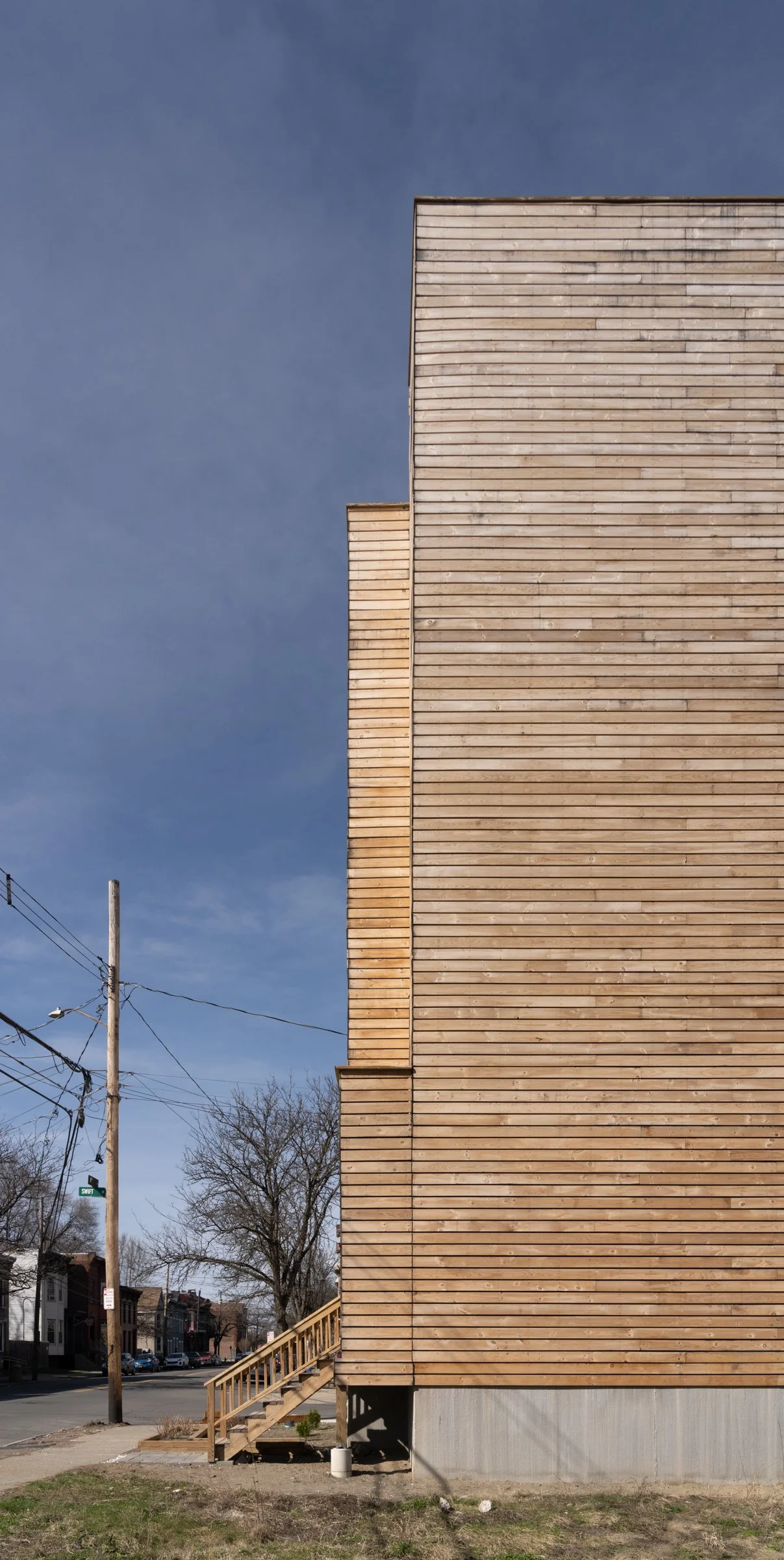 Side elevation of Swift Street Residences in Troy, New York, showing the vertical wood cladding and stepped entry stair.