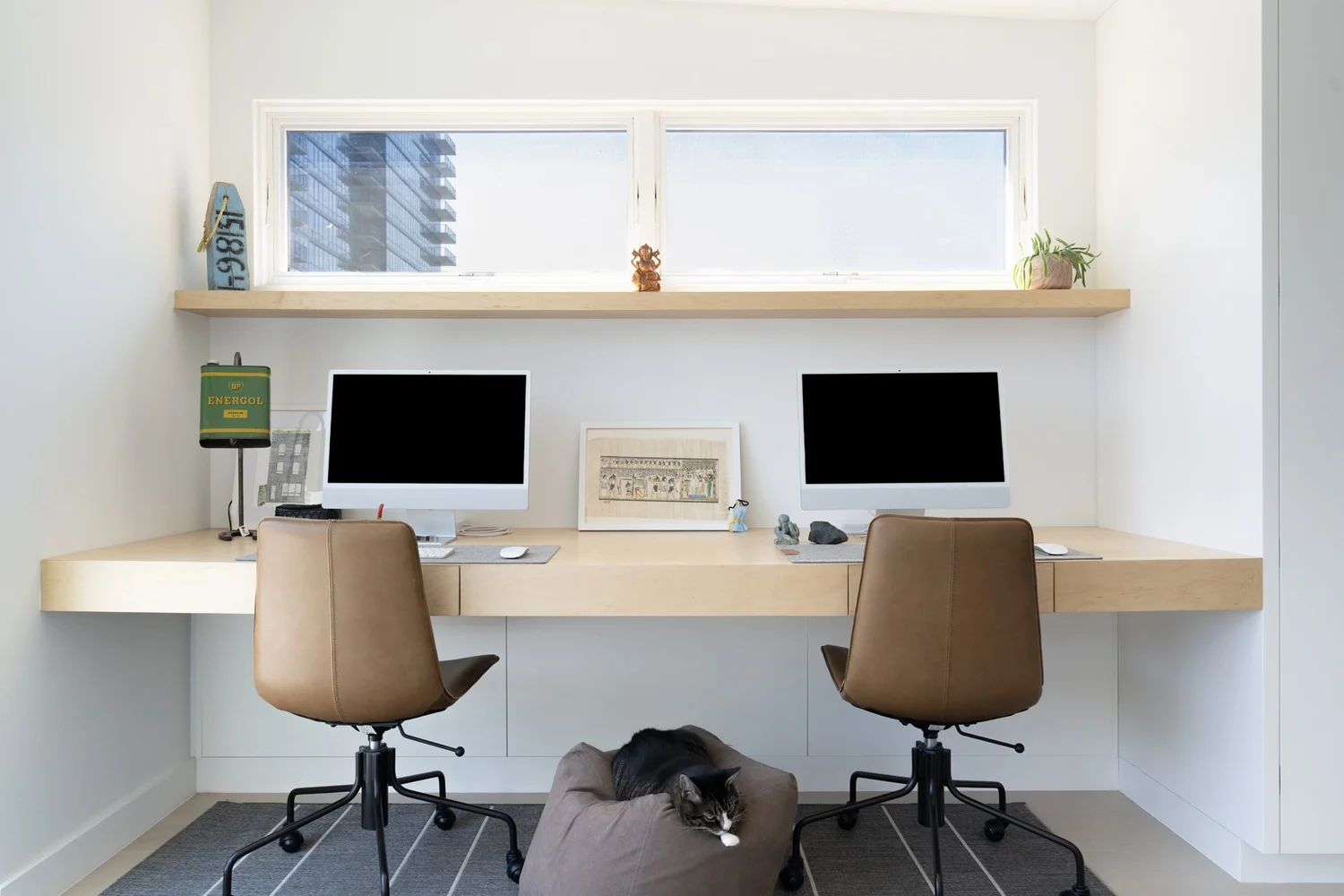 Custom built-in home office at Narrow Townhouse with two workstations, floating wood desk and shelf, leather chairs, and a cat resting on a cushion.