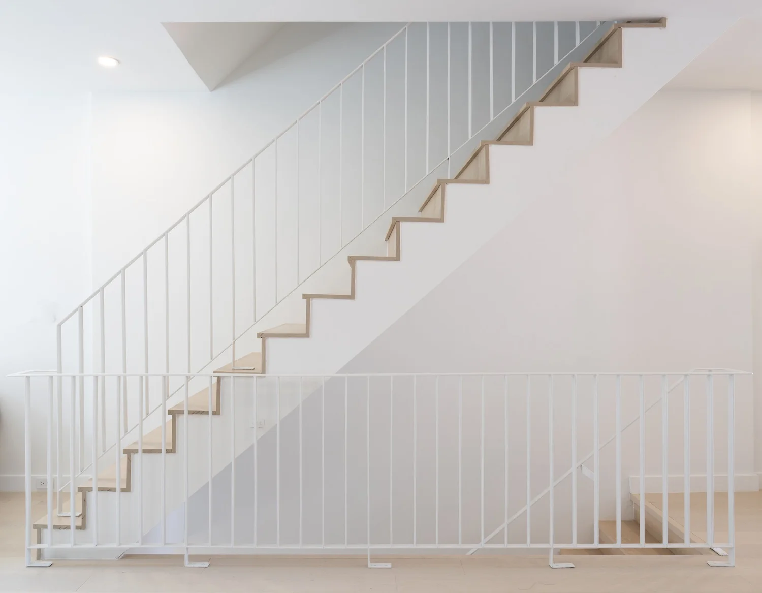 Side elevation view of Narrow Townhouse staircase with light wood treads and minimalist white metal railing against a clean white wall.