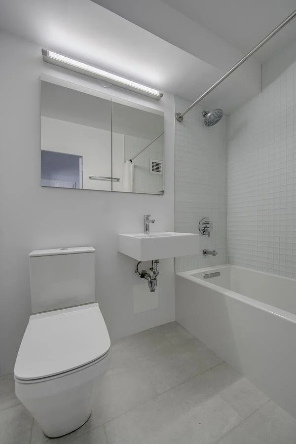 Minimalist bathroom in Harlem Studio with white tile, integrated mirror cabinet, bathtub-shower combination, and compact vanity sink.