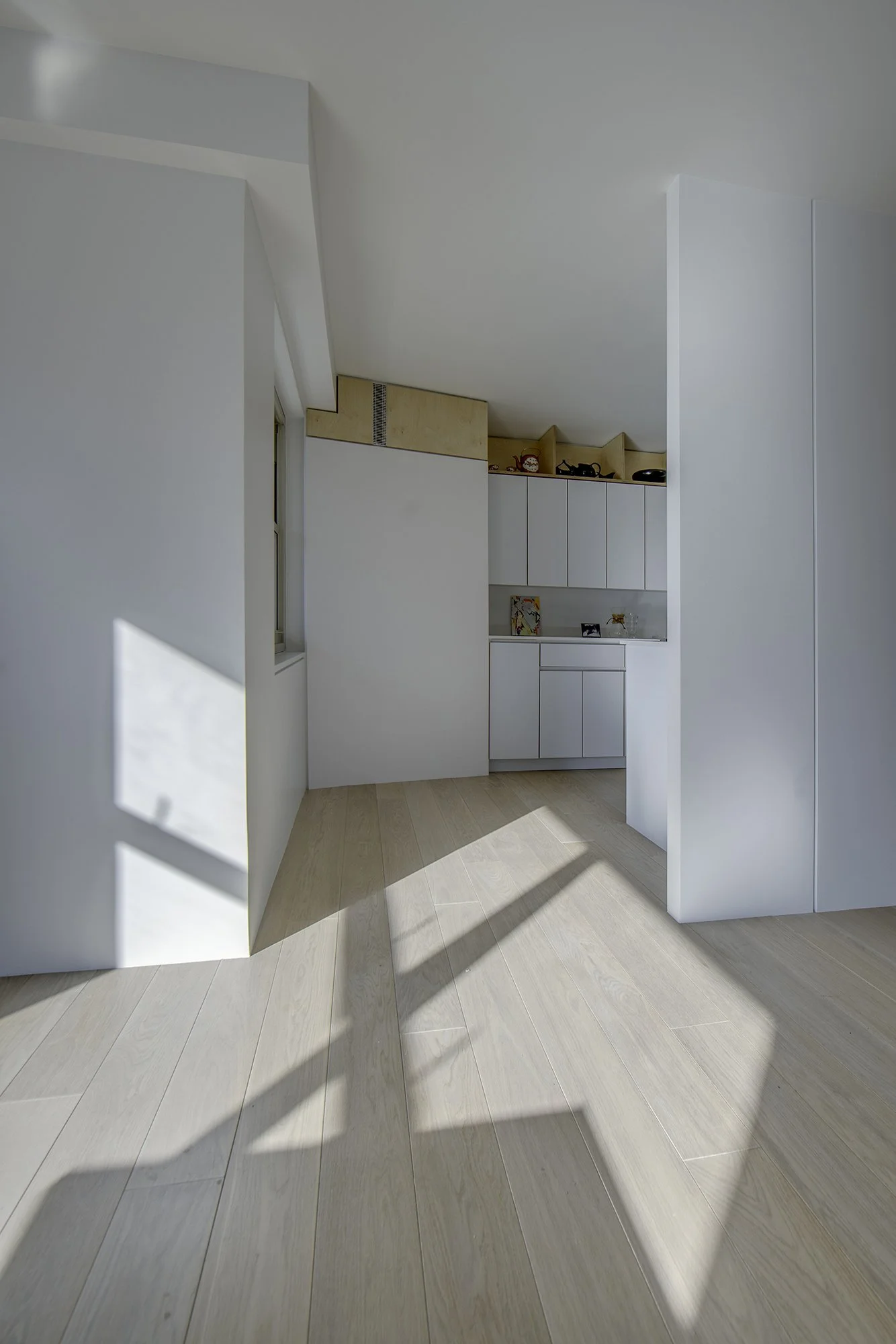Custom built-in shelving and storage units in Harlem Studio, with white cabinetry and open niches above, finished in light wood and white surfaces.