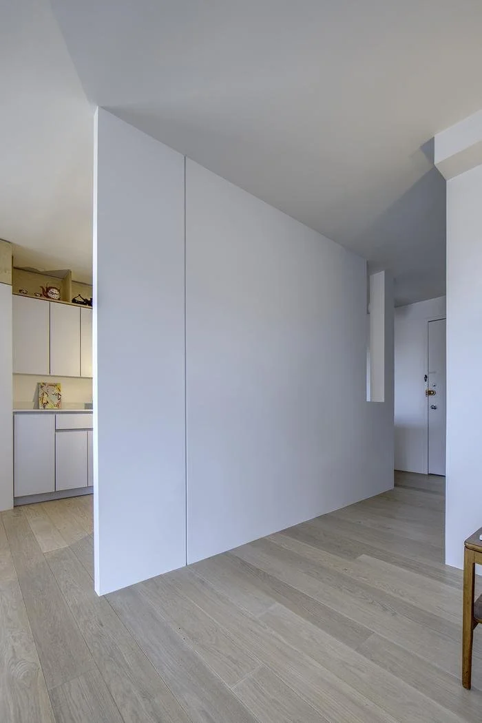 Minimalist white partition wall in Harlem Studio, creating separation between kitchen and entry while maintaining an open floor feel.
