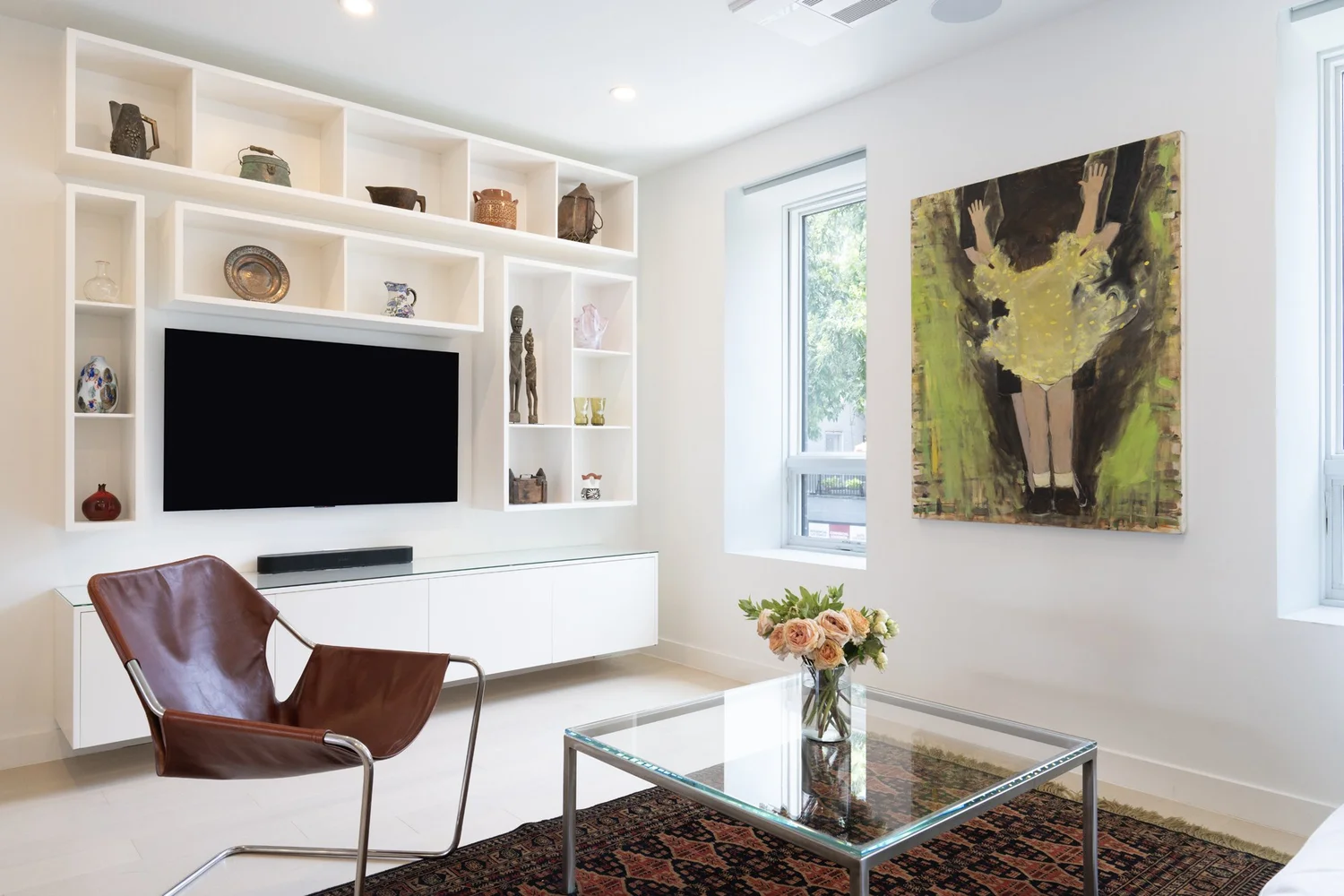 Living room interior at Narrow Townhouse featuring custom white built-in shelving, wall-mounted TV, contemporary artwork, and leather accent chair.