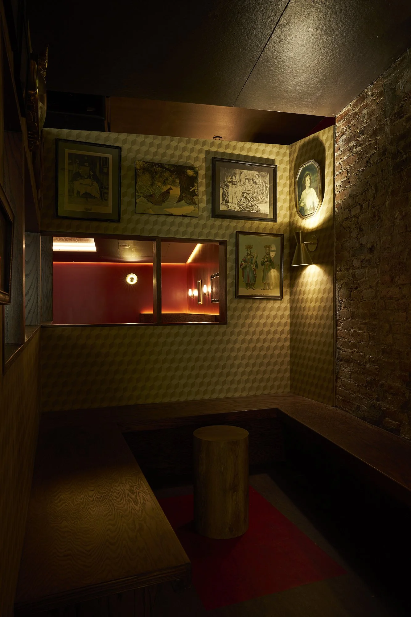 Booth seating area at Mr. Nancy’s with framed artwork, patterned wallpaper, exposed brick wall, and intimate lighting.