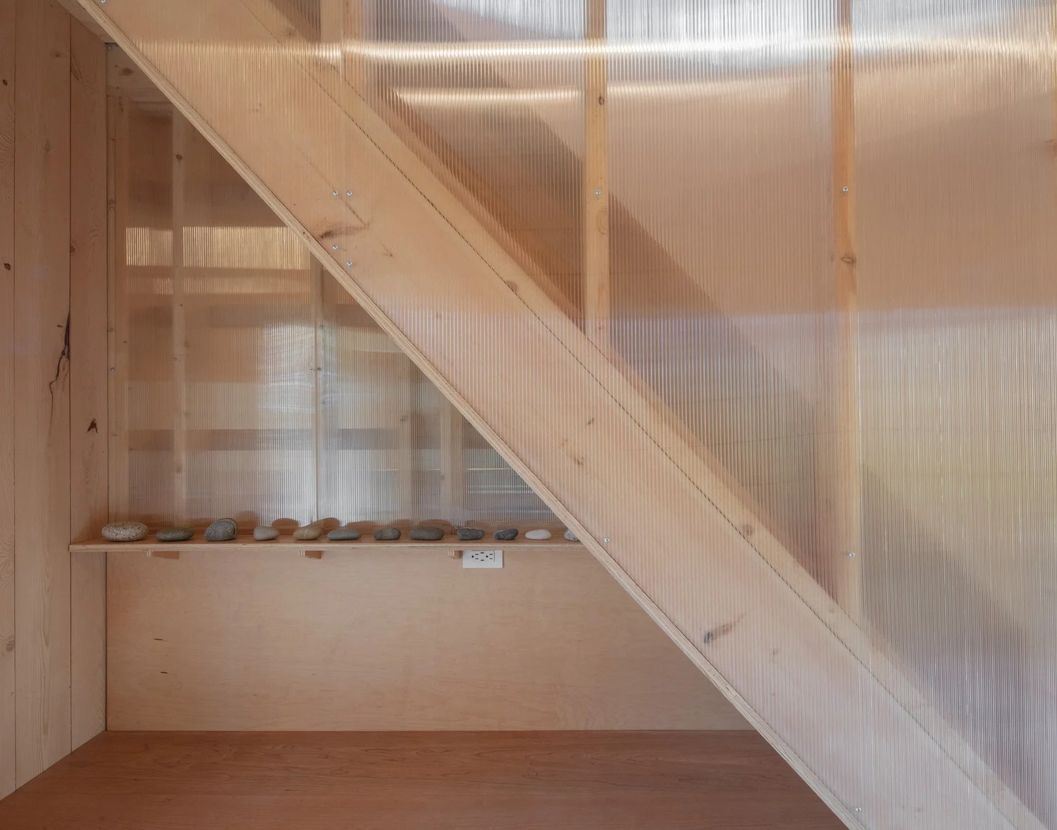 Detail of Barnard Barn stair enclosure. A wooden stair rises beside a translucent polycarbonate wall, with a built-in bench and wood finishes visible at the base.