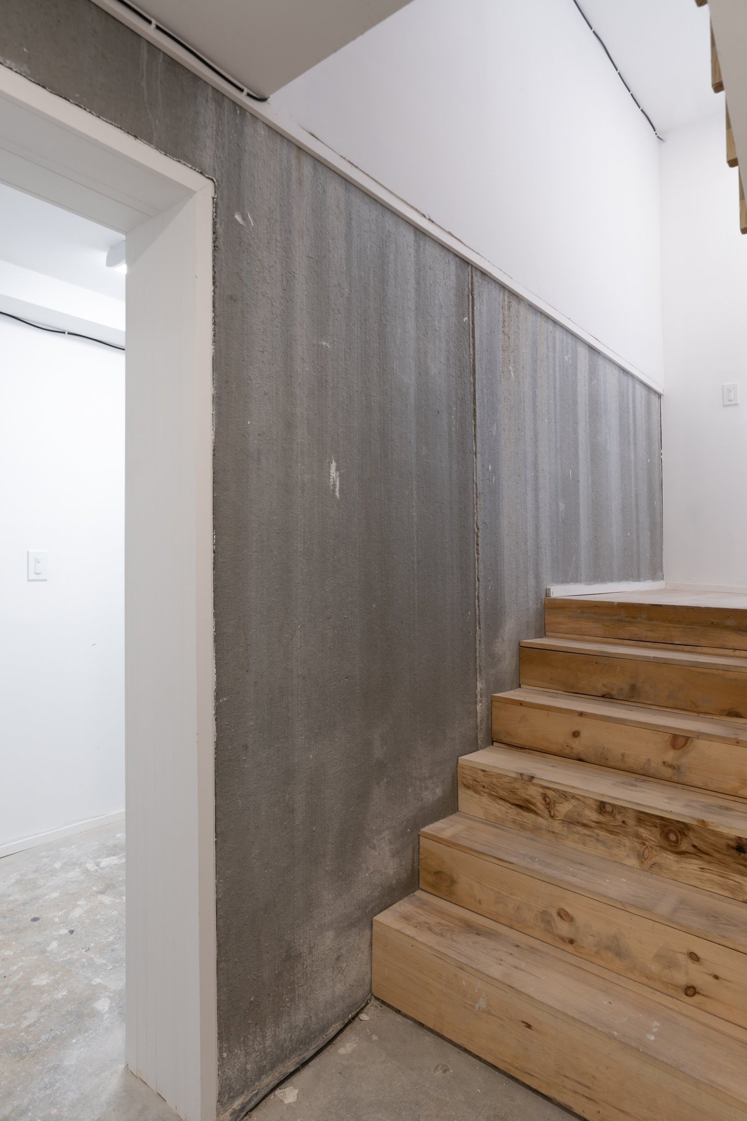 Unfinished interior stair detail at Swift Street Residences, showing raw wood steps adjacent to concrete and white plaster walls.