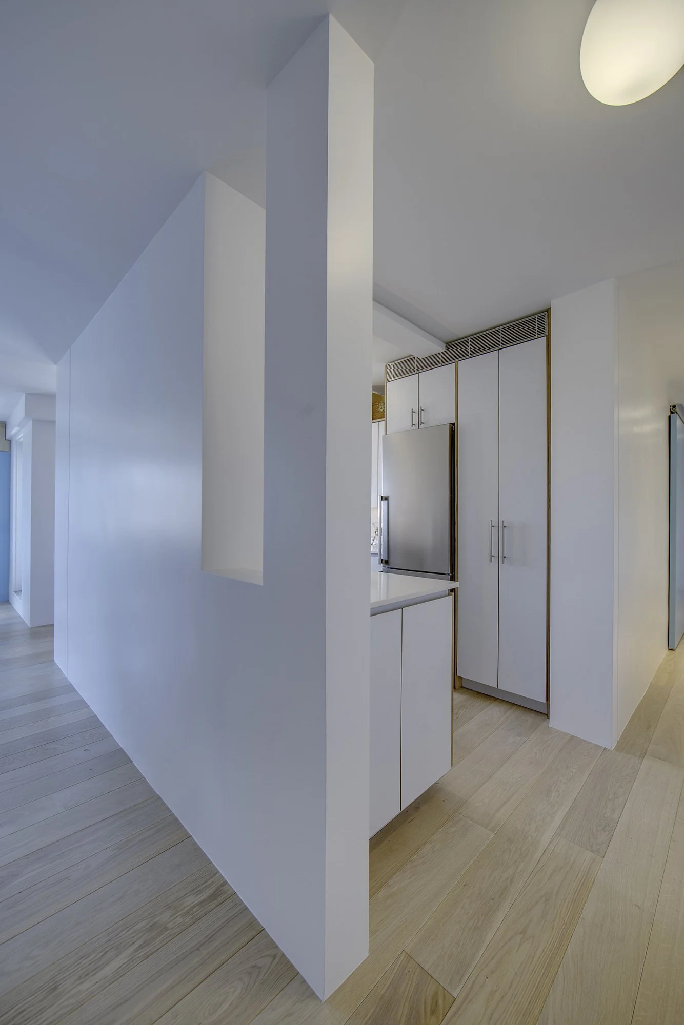 Harlem Studio kitchen concealed behind a minimalist white partition wall, featuring custom white cabinetry and integrated storage.