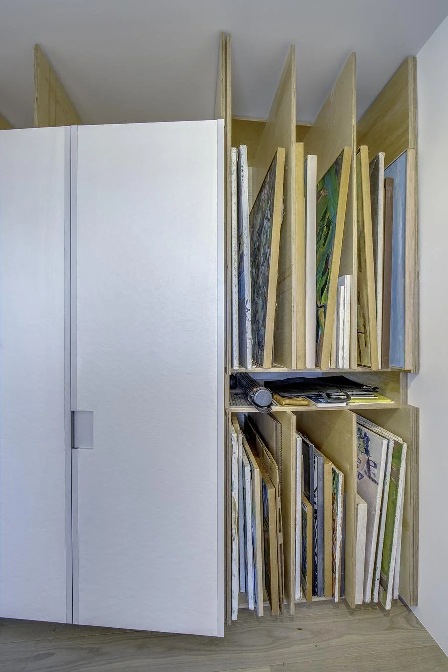 Detail view of Harlem Studio art storage system showing vertical wooden slots for organizing canvases and artwork beside sliding white panels.