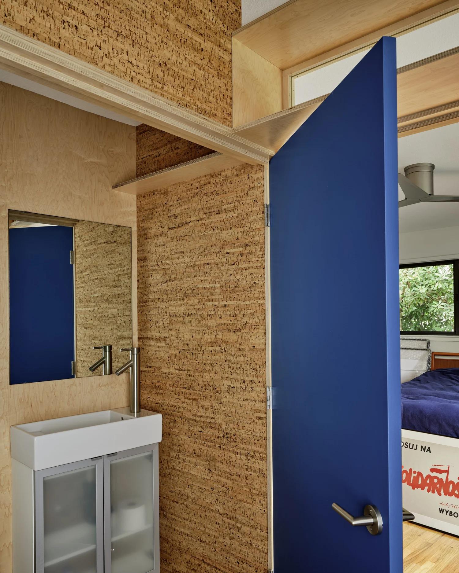 Bathroom entry at Three Cork Walls featuring a blue door, cork wall surfaces, and a small vanity sink with a wall-mounted mirror.
