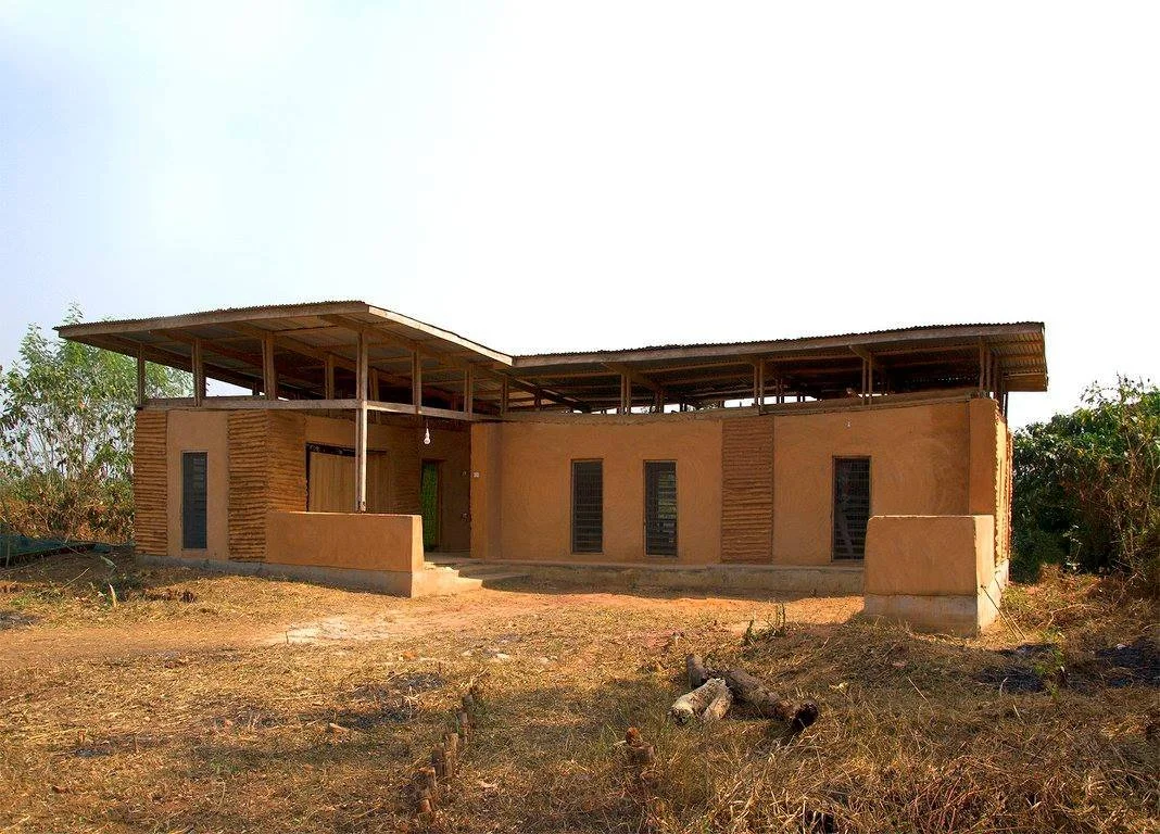 Front view of the Mudhouse showing earthen walls, shaded corrugated roof, and natural ventilation design.