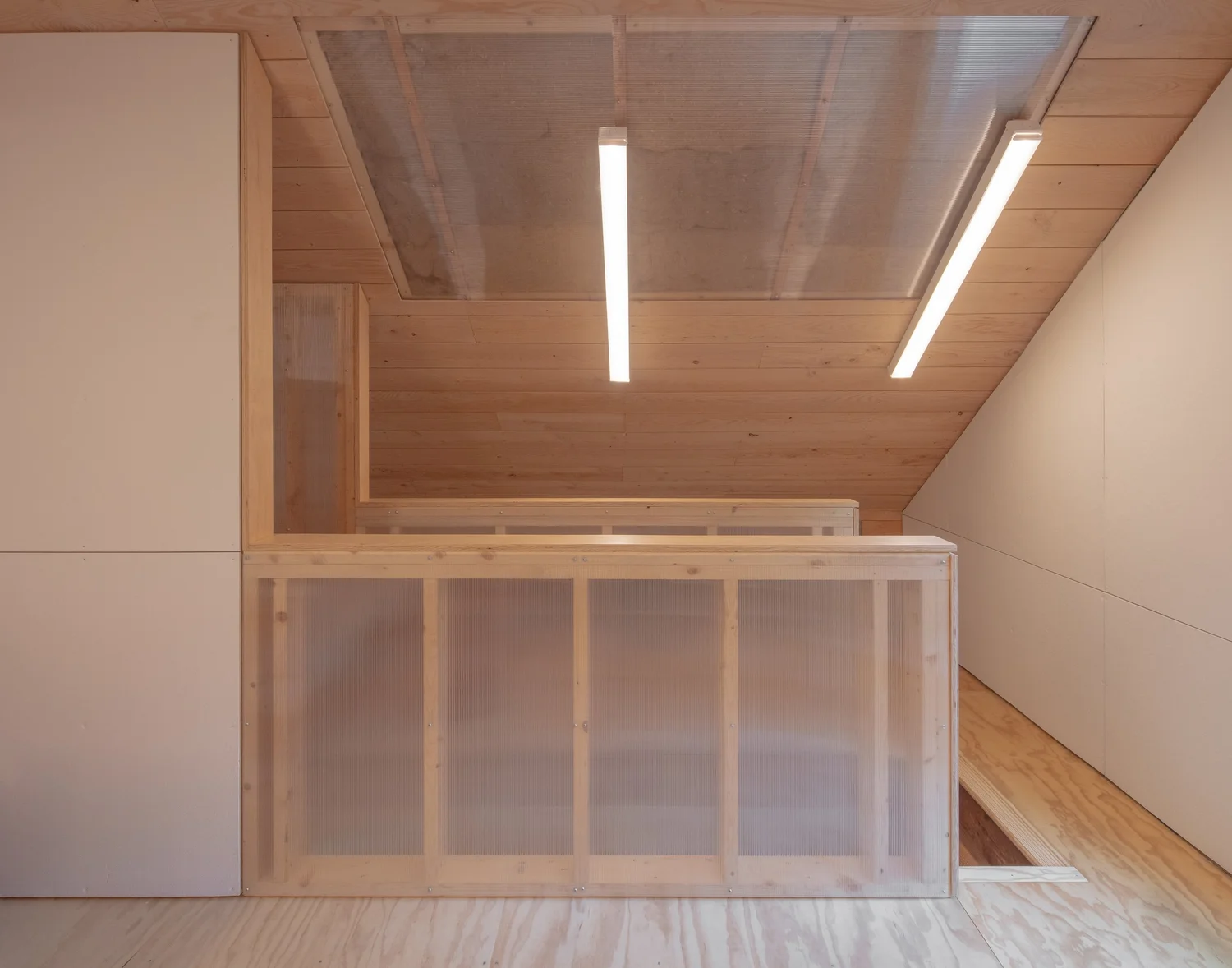 Interior view of Barnard Barn loft showing wood floors, Homasote wall panels, and a translucent polycarbonate guardrail with overhead linear lighting.
