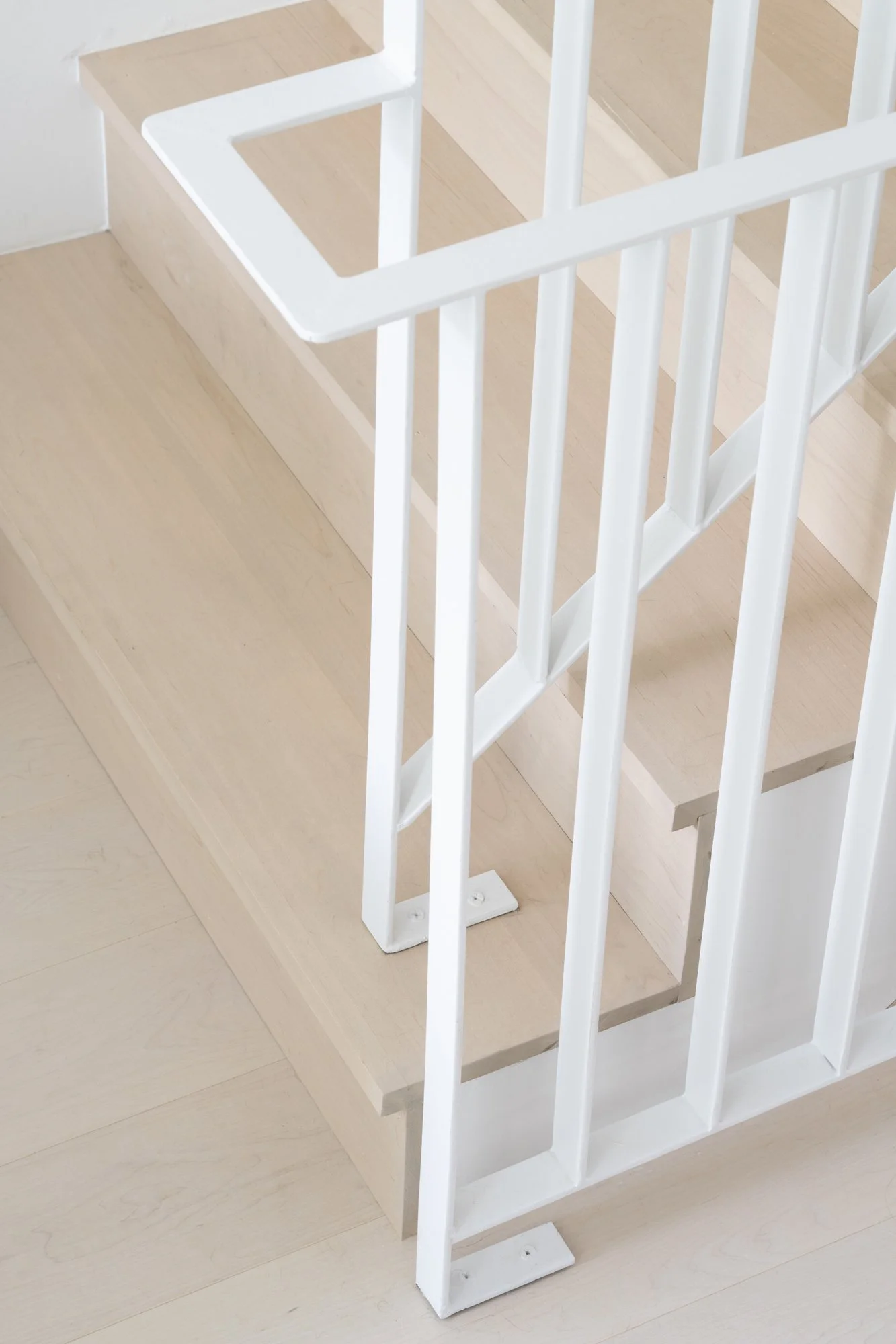 Detail of Narrow Townhouse staircase showing light wood steps and white metal railing connection.