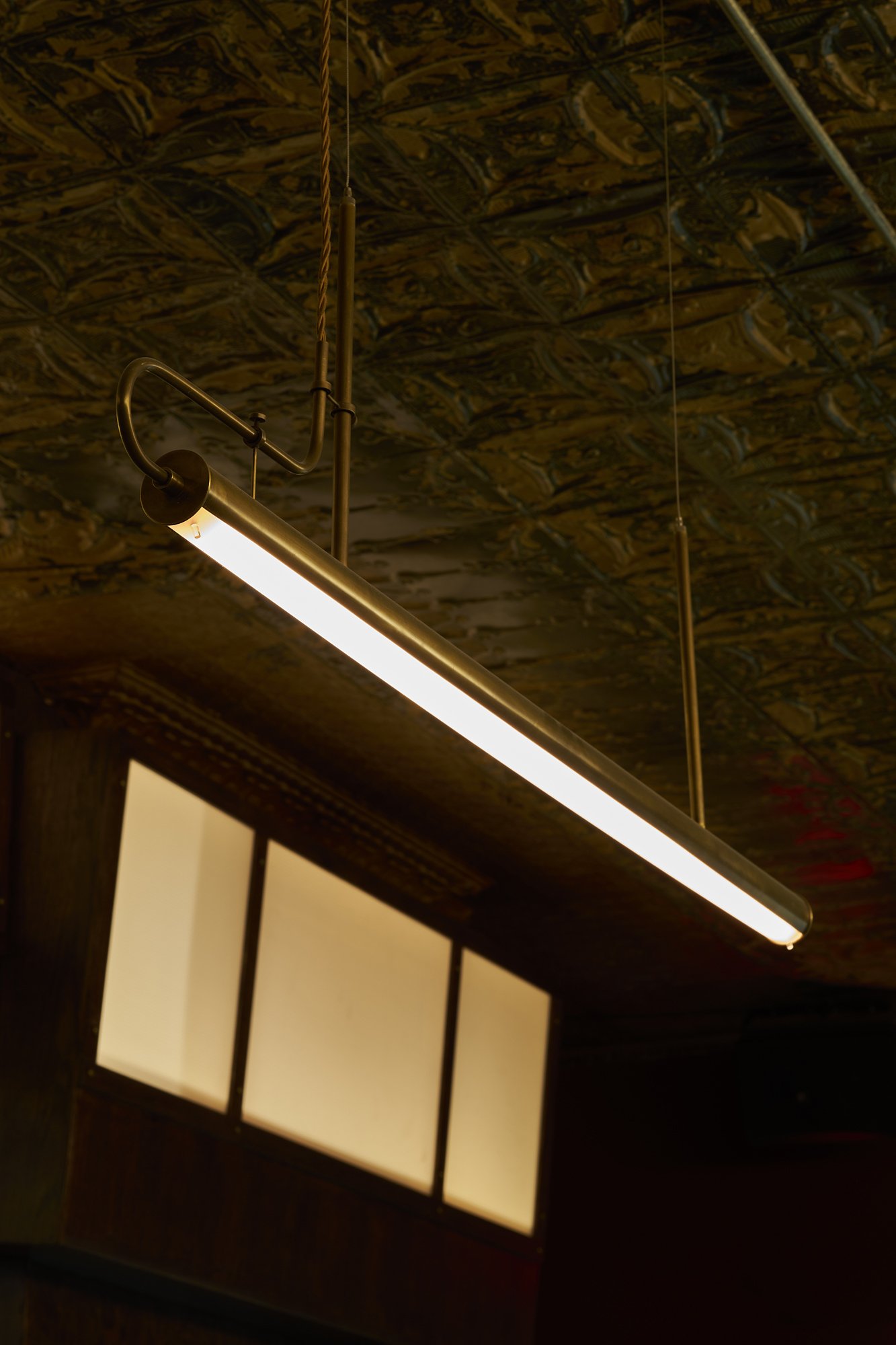 Pendant light fixture at Mr. Nancy’s bar, suspended from a tin ceiling above frosted glass panels.