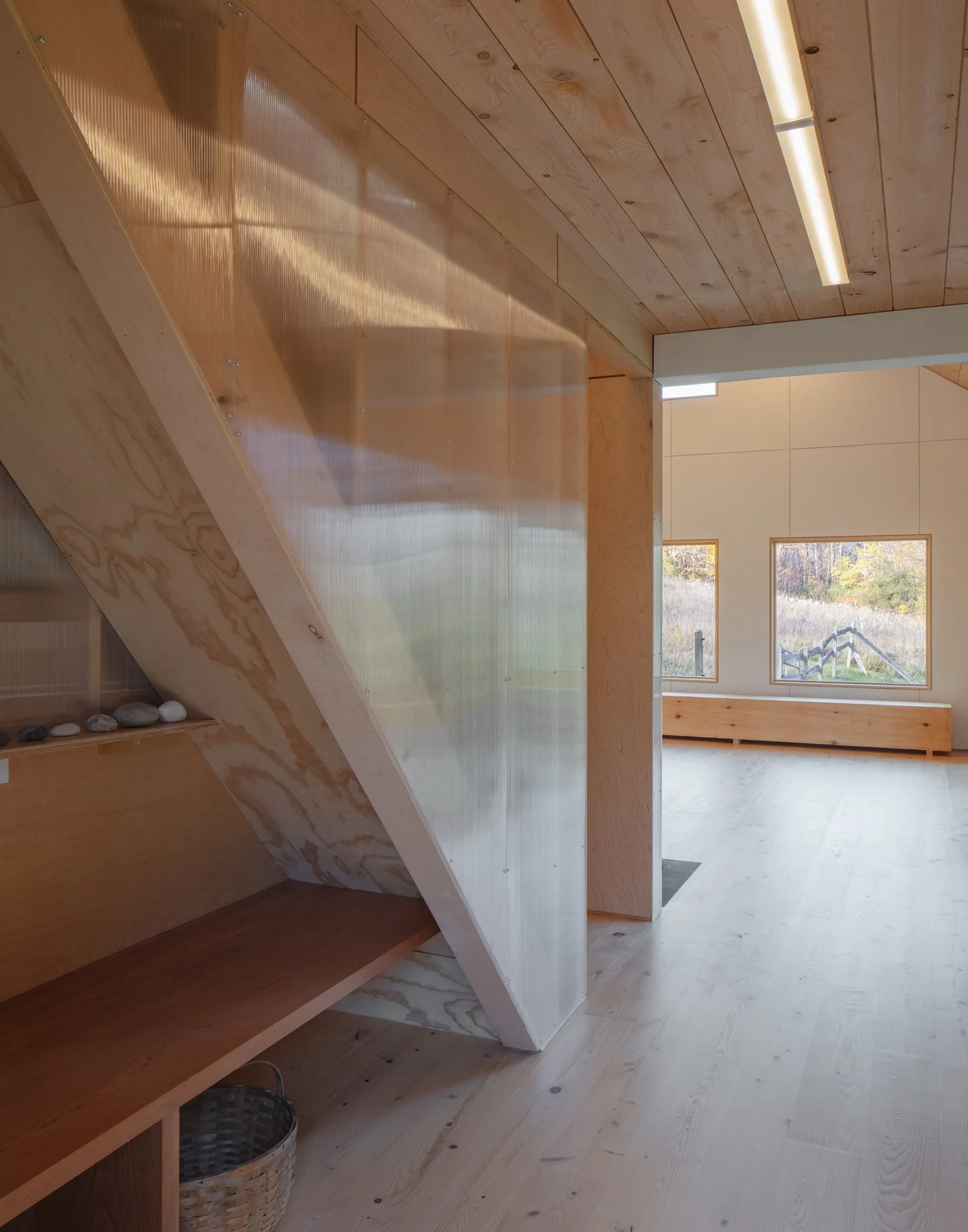 Interior detail of Barnard Barn showing a built-in wooden bench beneath a stair with a slanted plywood enclosure, opening into the main hall.