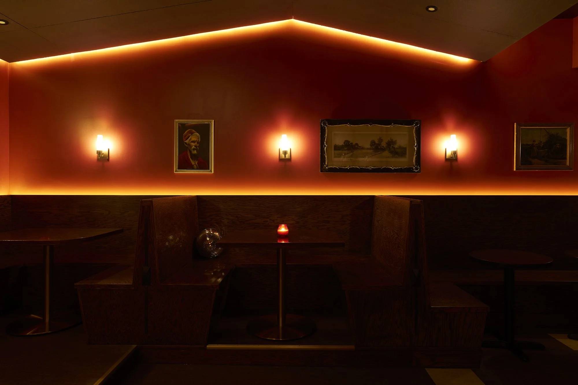 Warm red lighting highlights the façade of a bar with framed artwork.