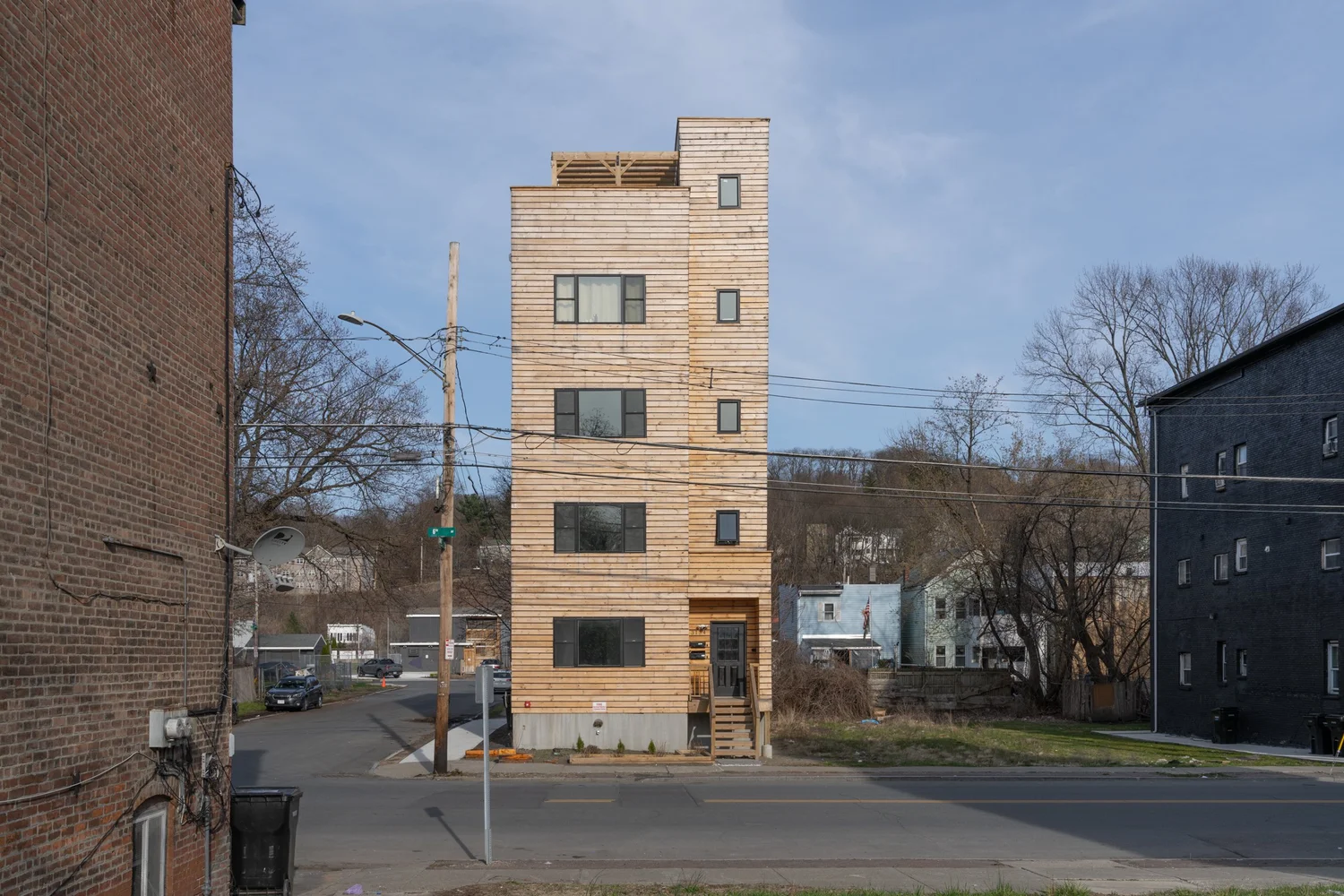Full street view of Swift Street Residences in Troy, New York, a narrow four-story wood-clad infill housing building between existing brick structures.