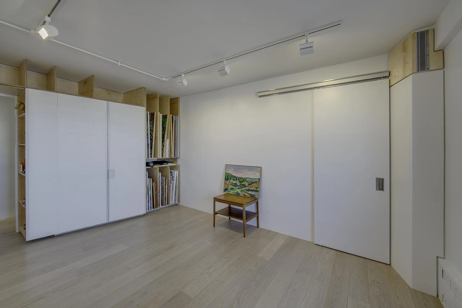 Custom art storage wall in Harlem Studio with large sliding white panels, open wood shelving, and vertical slots for canvases and artwork.