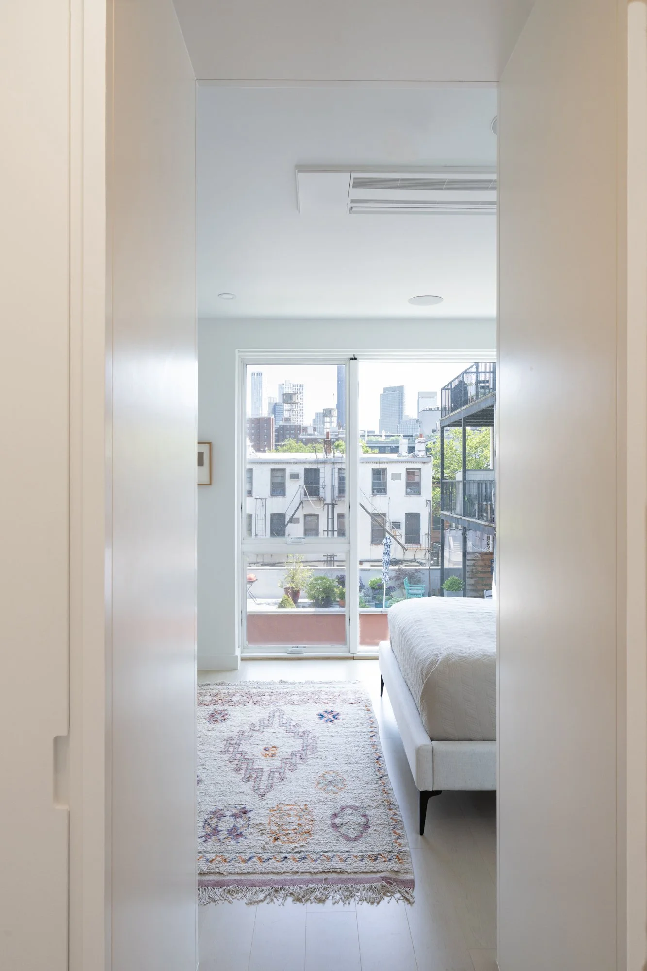 Bedroom at Narrow Townhouse with floor-to-ceiling windows opening to a terrace, featuring a patterned rug and city views.