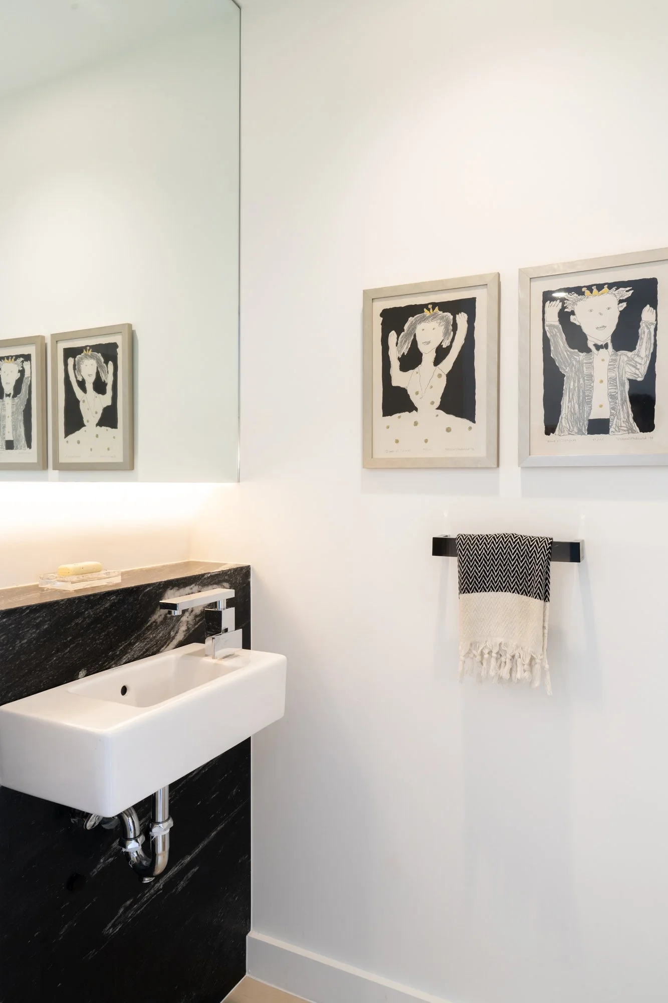 Powder room at Narrow Townhouse with wall-mounted sink, black marble counter, towel rack, and framed artwork.