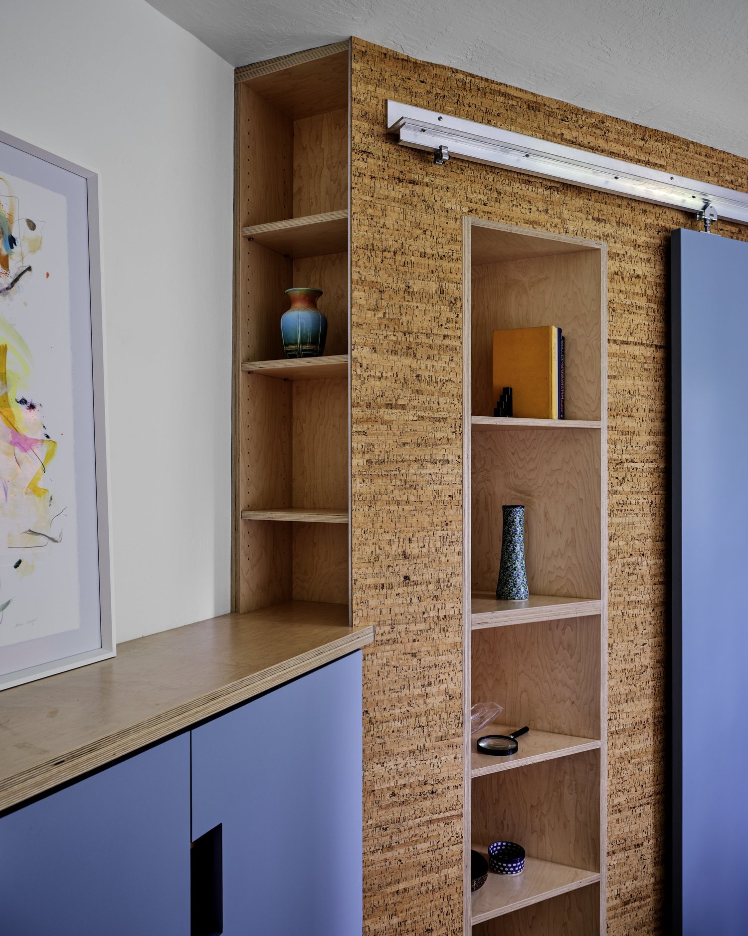 Built-in shelving clad in cork wall panels at Three Cork Walls, integrated with adjacent blue cabinetry and natural wood surfaces.