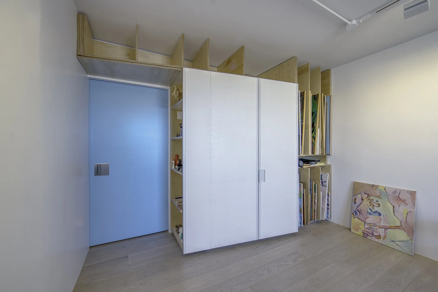 Custom blue sliding door in Harlem Studio integrated with built-in white cabinets and vertical plywood art storage slots.