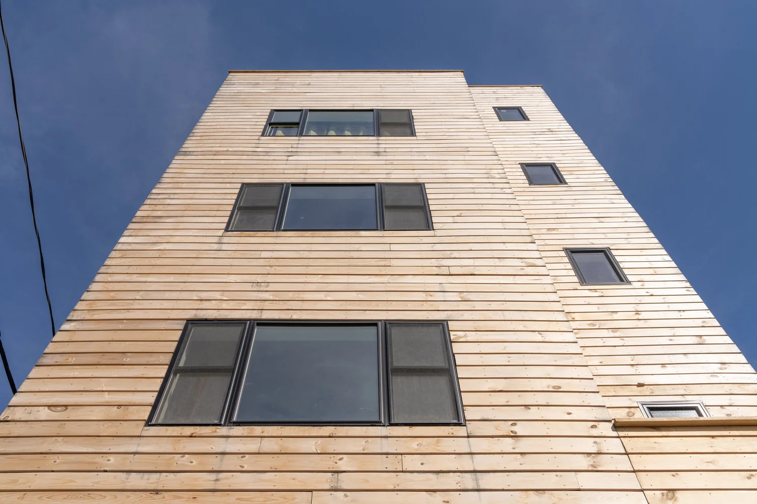 Close-up view of Swift Street Residences, highlighting the vertical wood cladding and large windows against a blue sky.