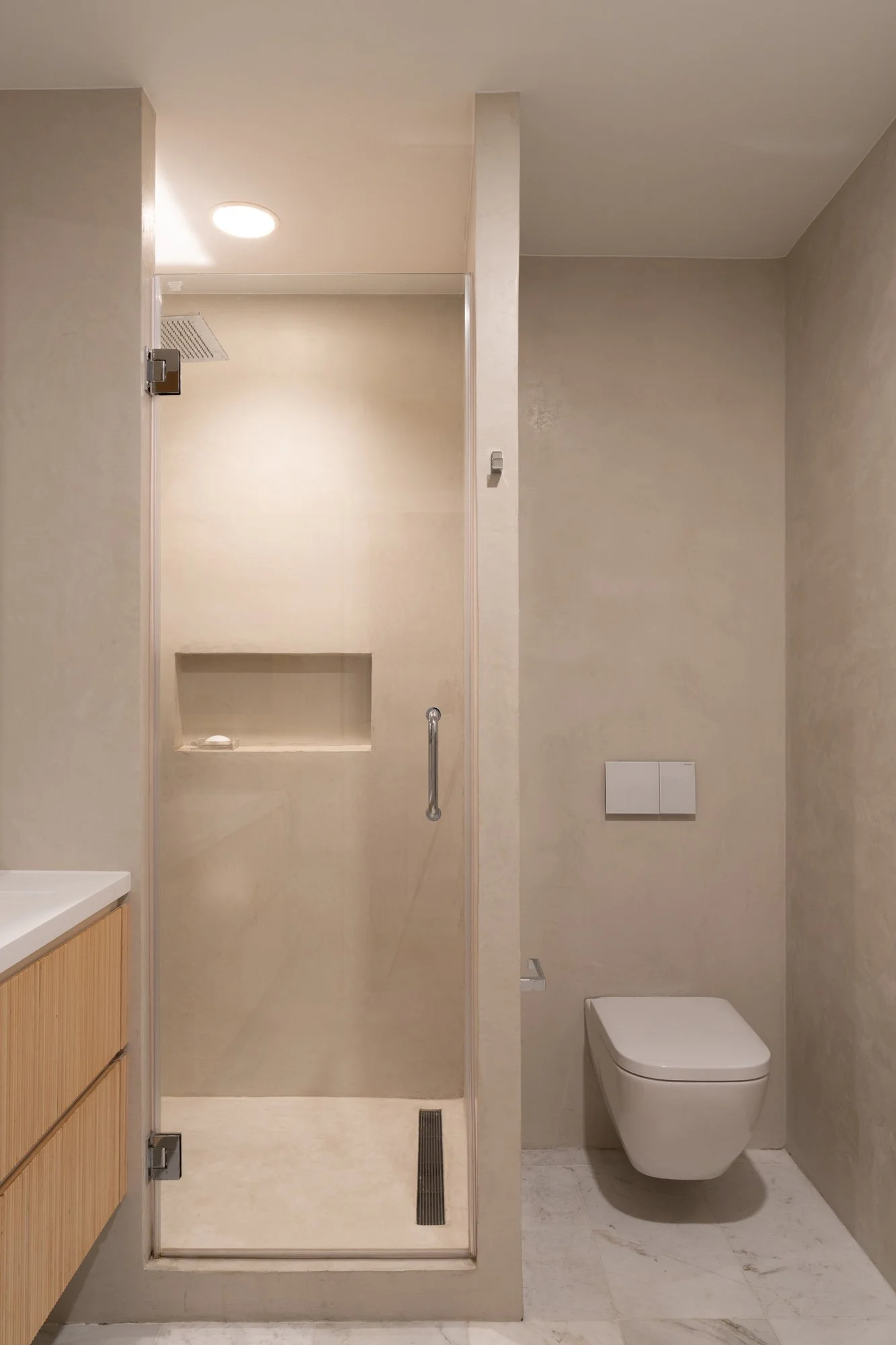 Bathroom interior at Narrow Townhouse featuring a minimalist walk-in shower with glass door, wall-mounted toilet, and light wood vanity.