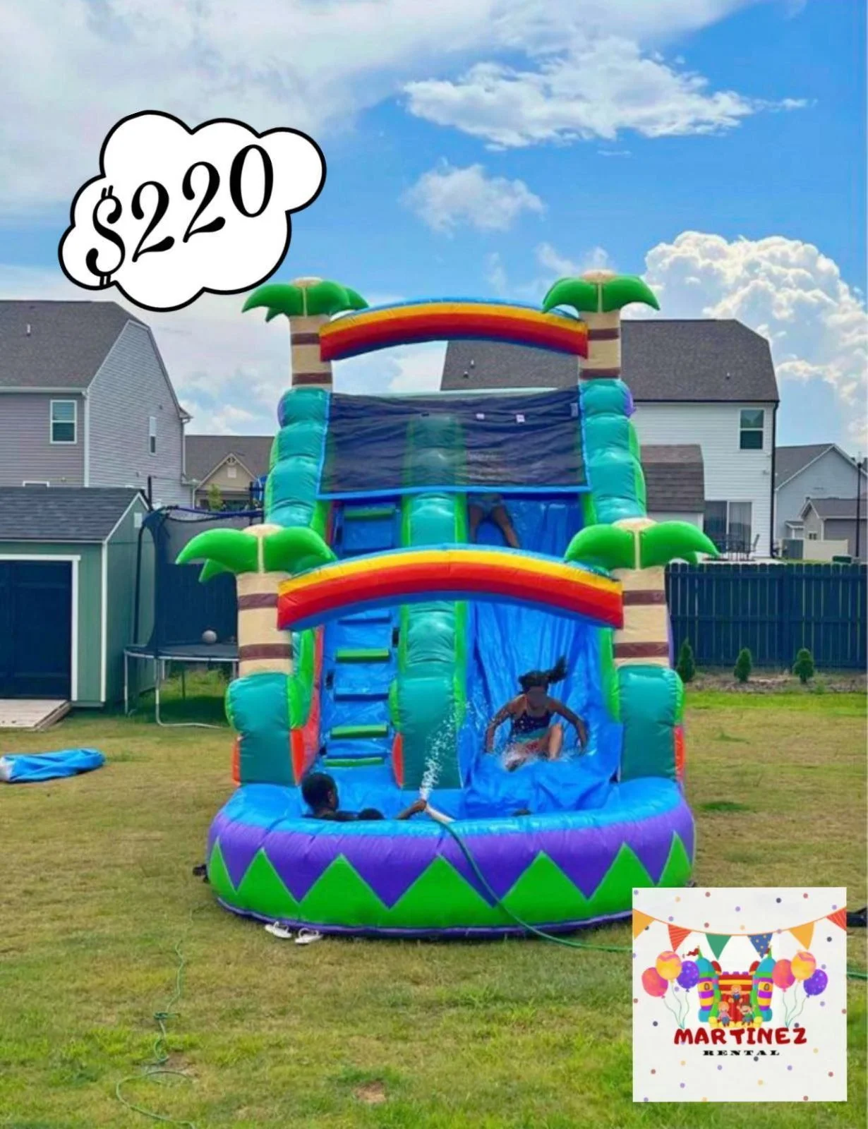 Colorful inflatable water slide in a backyard with children playing, trees, fences, and houses in the background, and a price tag of $220