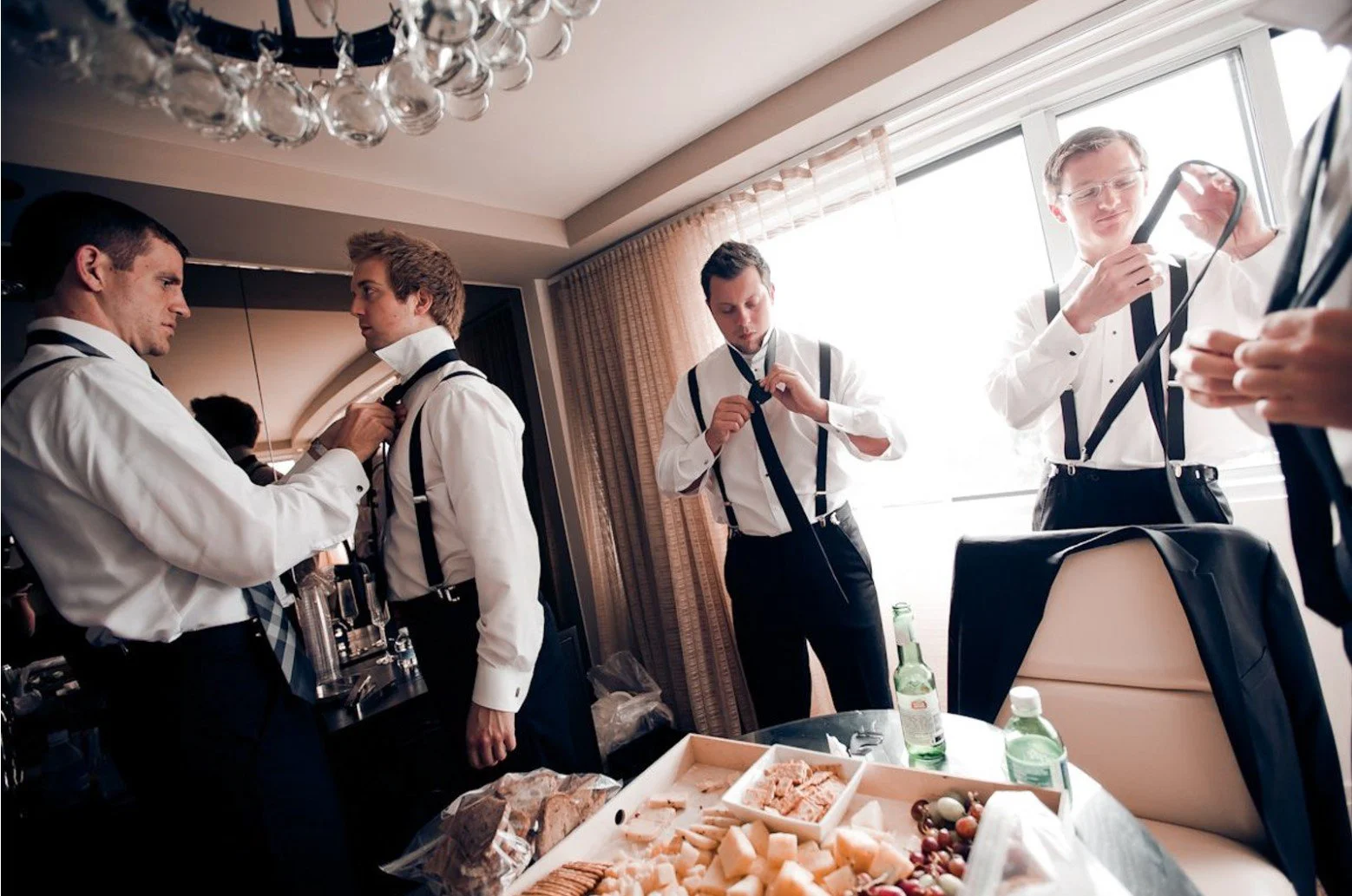 Groomsmen helping each other put on their ties in a hotel room.