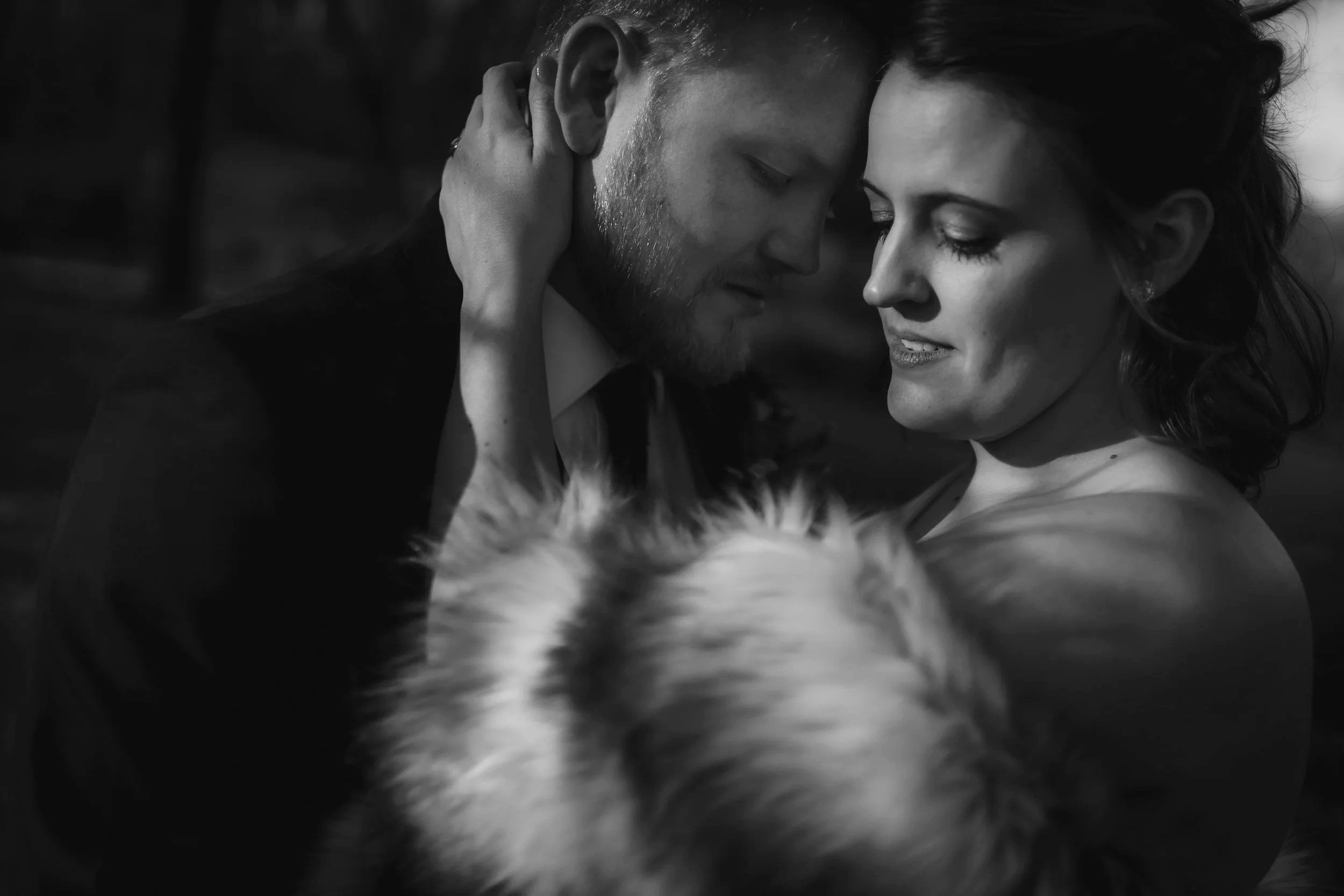 Black and white photo of a couple with a dog. The man and woman are close, touching foreheads, with the man's hand on the woman's neck. They appear to be in an intimate moment.