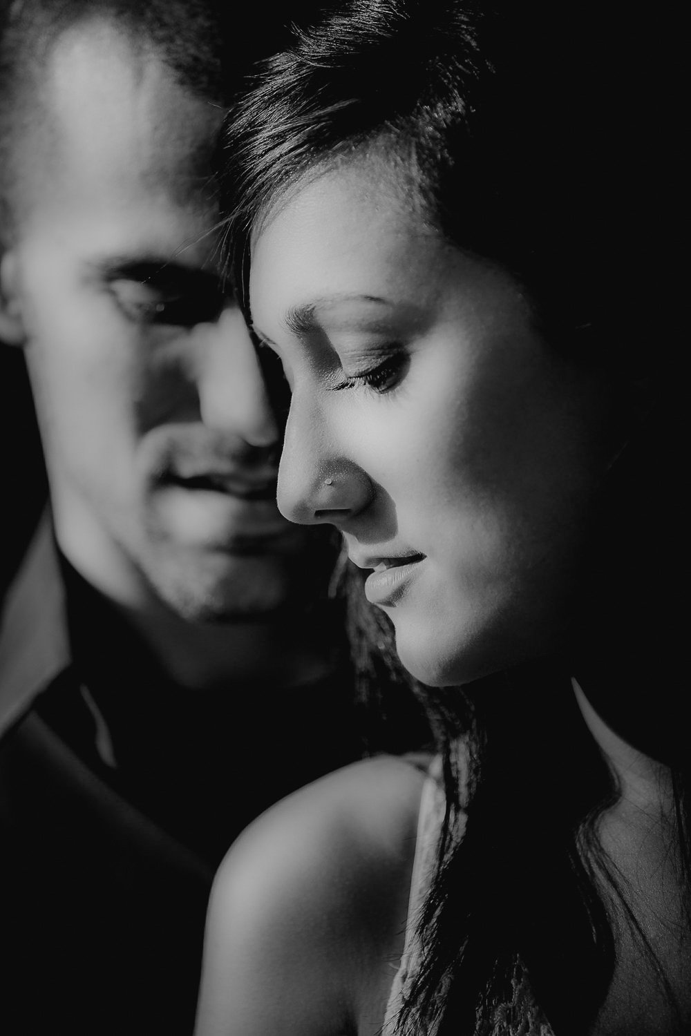 A black-and-white close-up photograph of a man and woman with their faces near each other, both with their eyes closed, conveying intimacy.