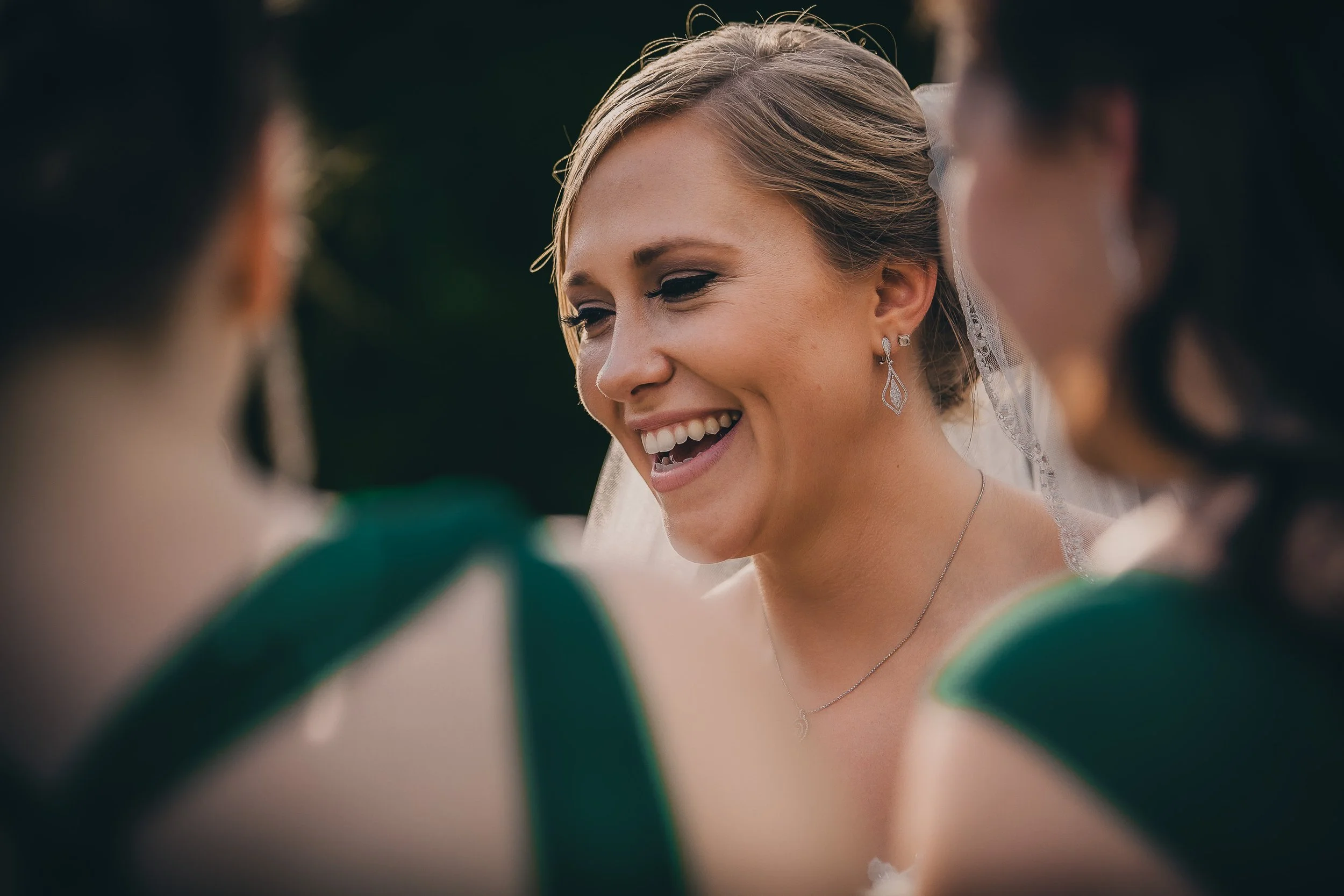 A bride smiling happy during a wedding ceremony surrounded by bridesmaids wearing green dresses.