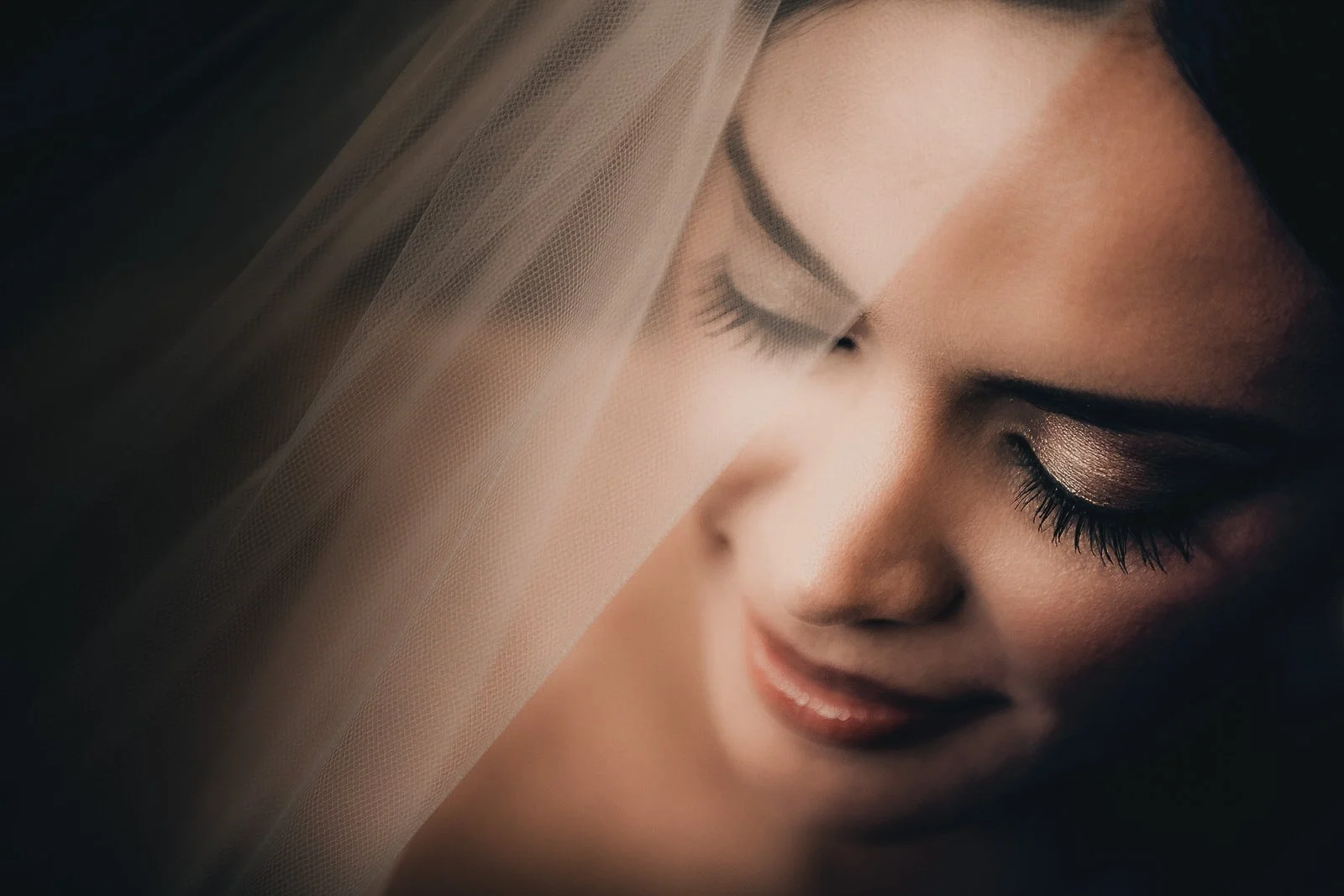 Close-up of a woman's face with closed eyes, wearing makeup, with a veil draped over part of her face.