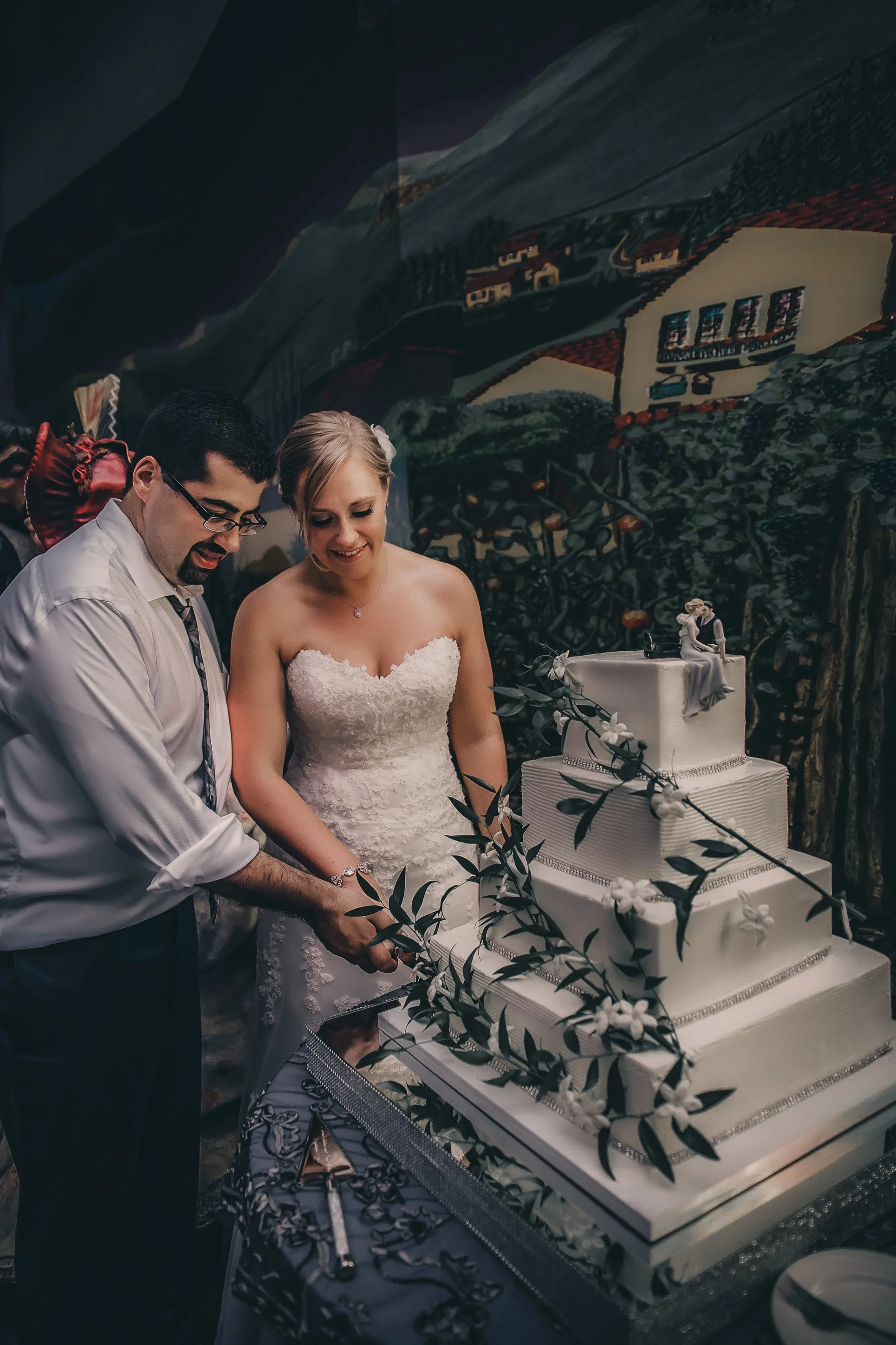 A bride and groom cutting a wedding cake together amid wedding decorations.