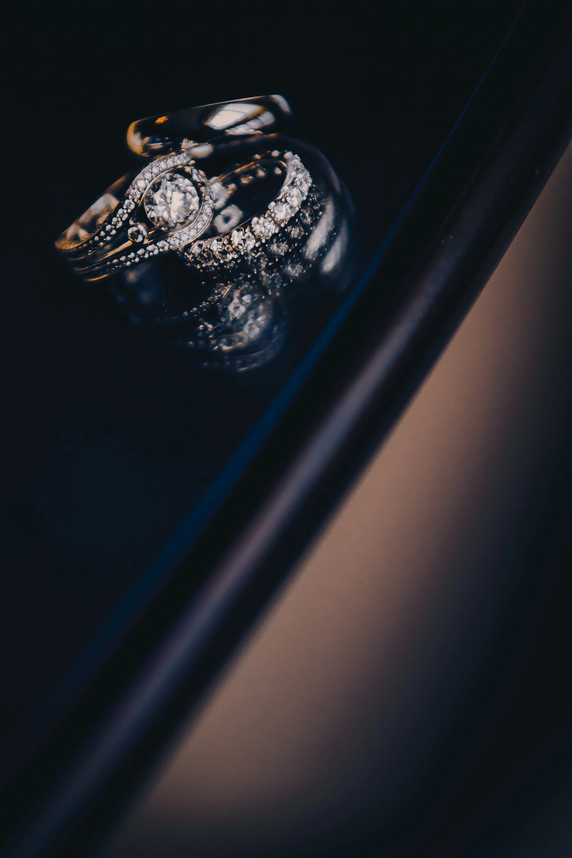 Close-up of three silver rings with diamonds on a black surface.